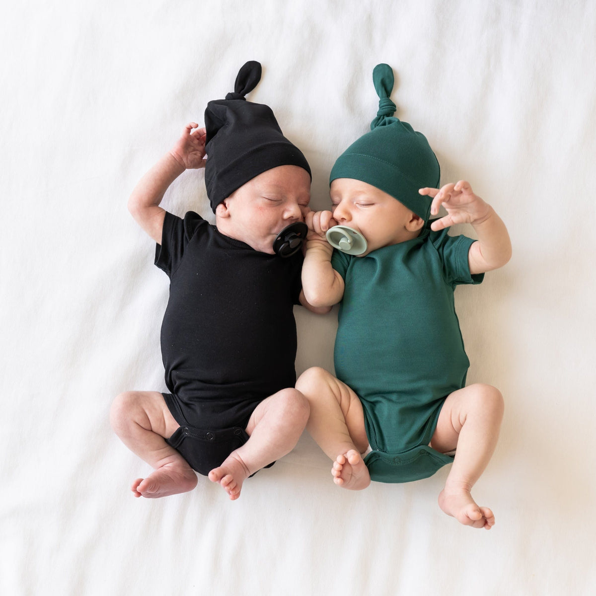 Newborns sleeping next to each other while wearing Knotted Caps and matching Short Sleeve Bodysuits in Midnight and Emerald