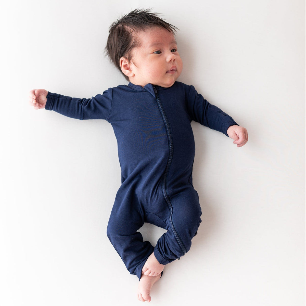 Infant laying in a crib while wearing a Zippered Romper in Navy