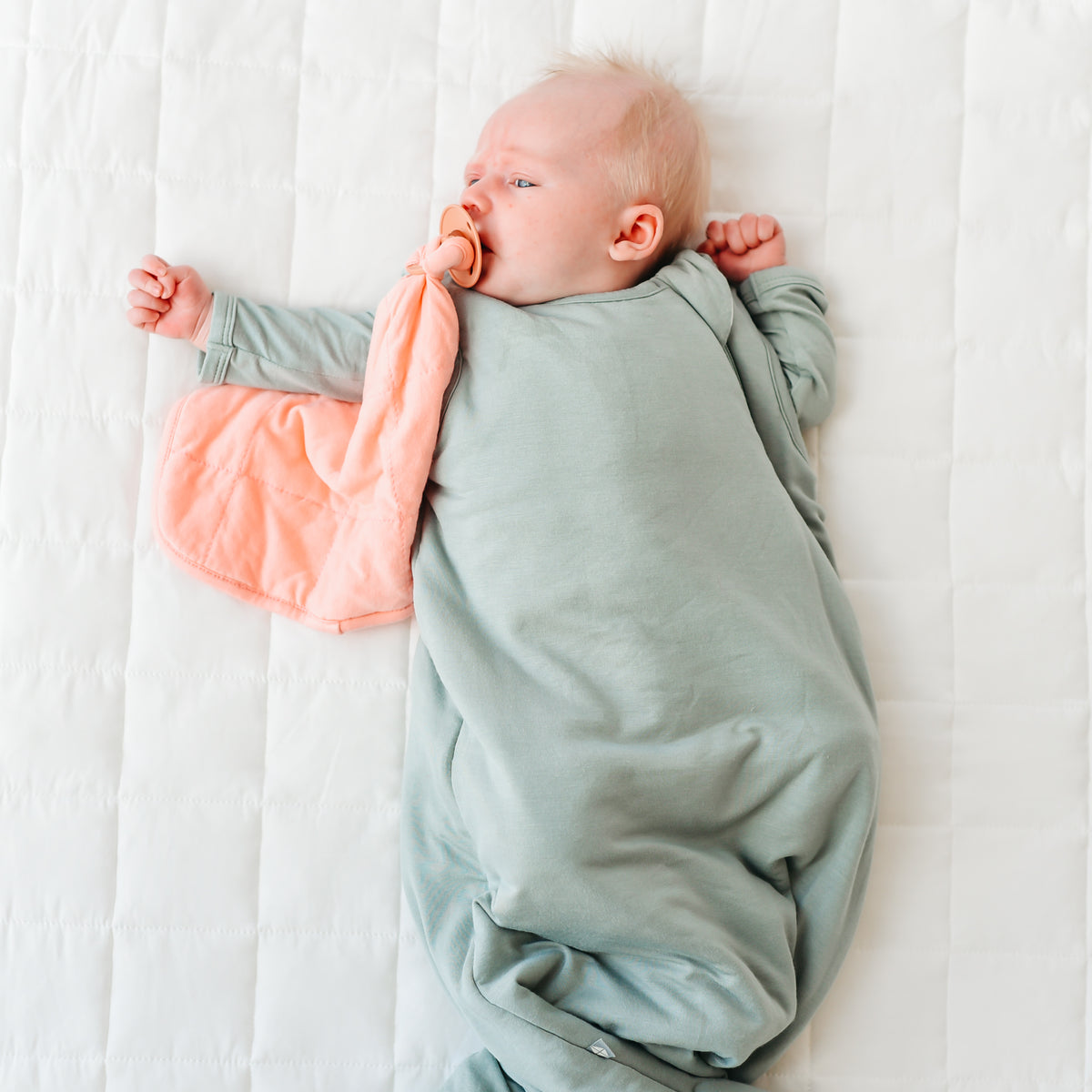 newborn baby sucking on pacifier attached to lovey