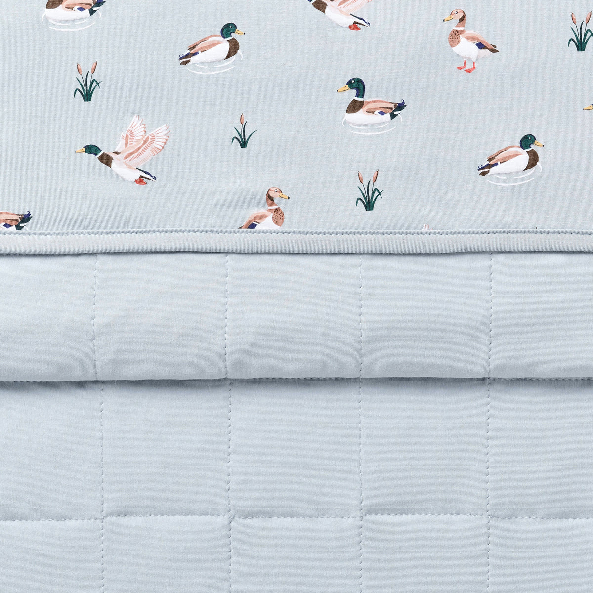 Close up of the Baby Blanket in Mallard Duck showing the quilted blue backing and patterned smooth top layer