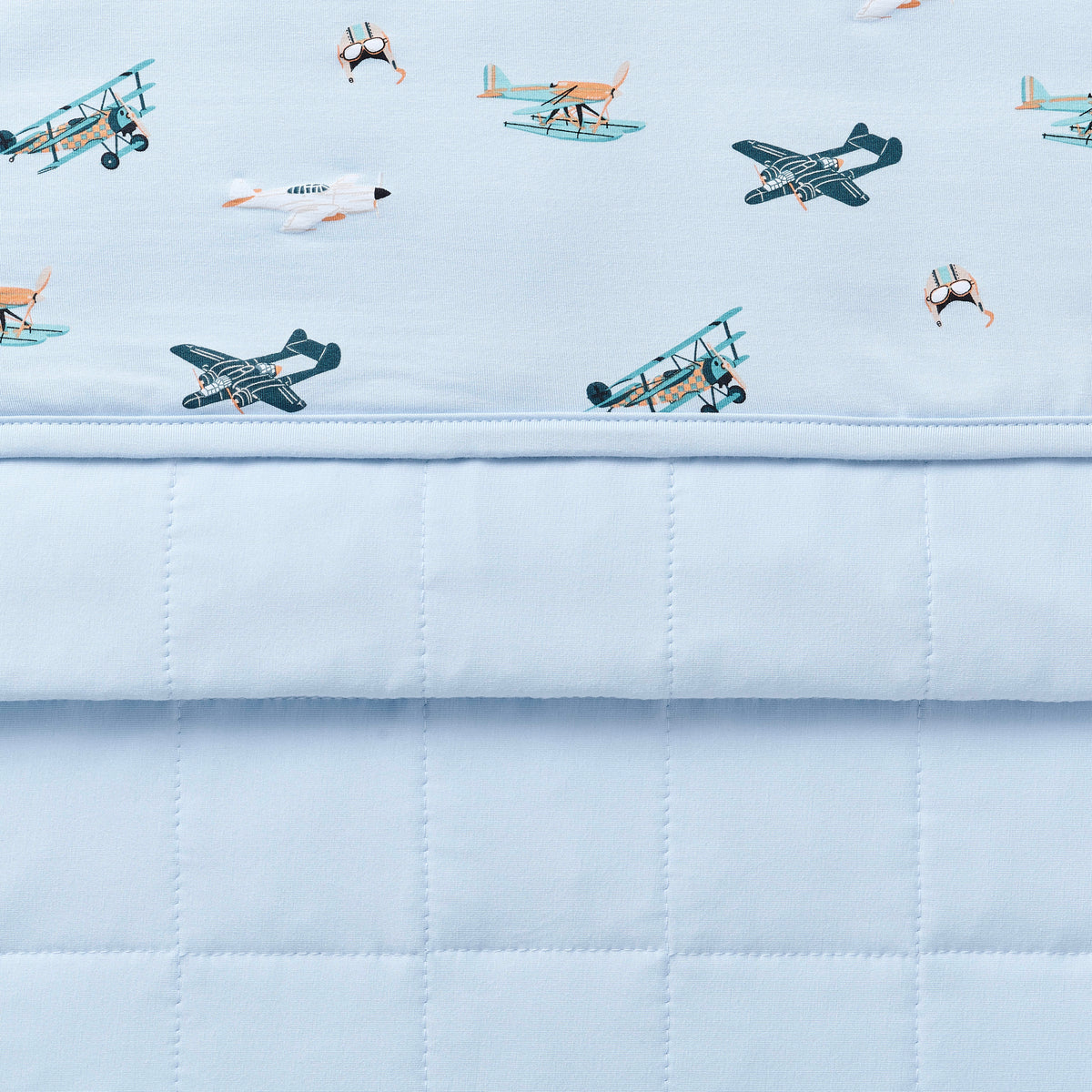 Close up of the Toddler Blanket in Take Off 1.0 showing the light blue quilted backing and plane print smooth top layer