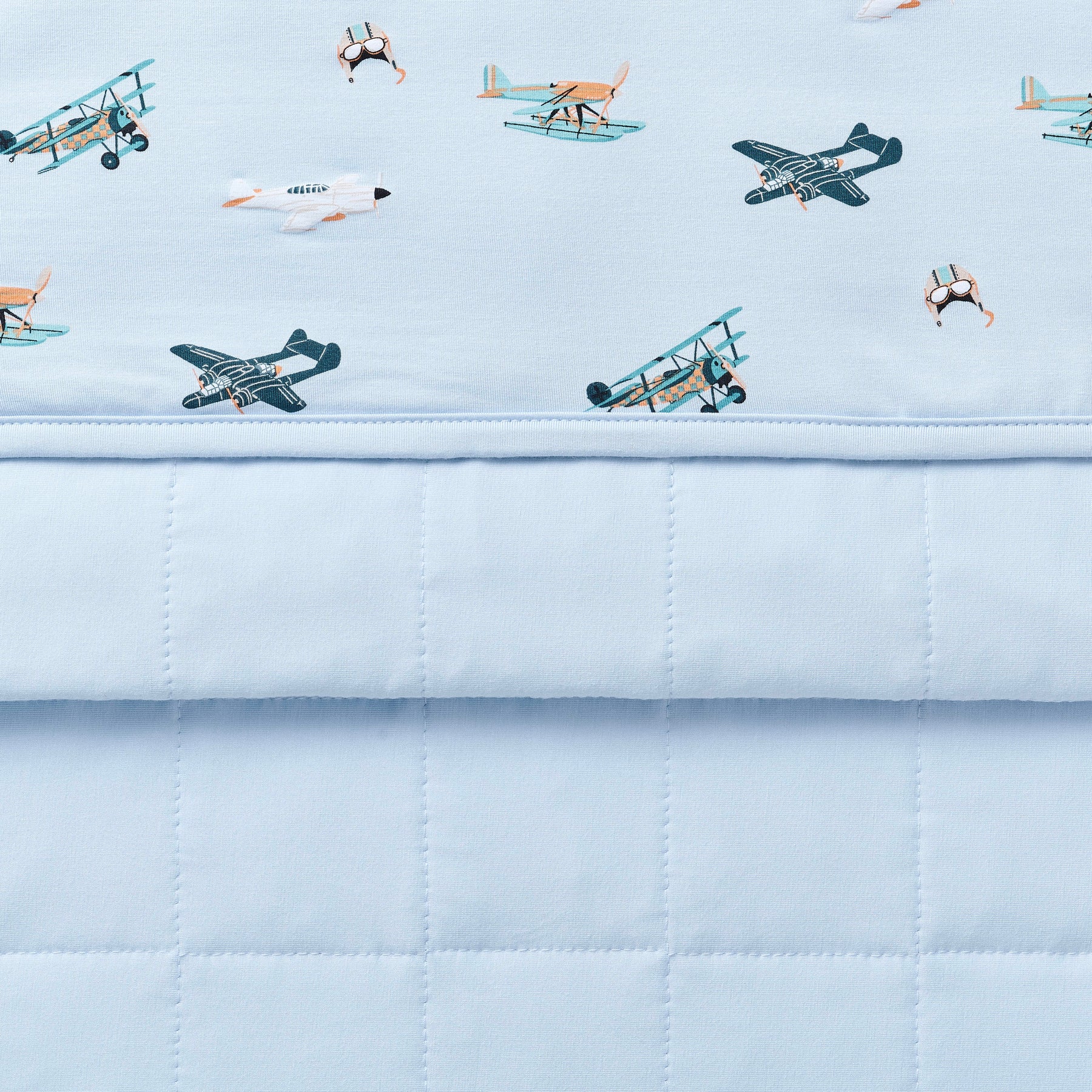 Close up of the Toddler Blanket in Take Off 1.0 showing the light blue quilted backing and plane print smooth top layer
