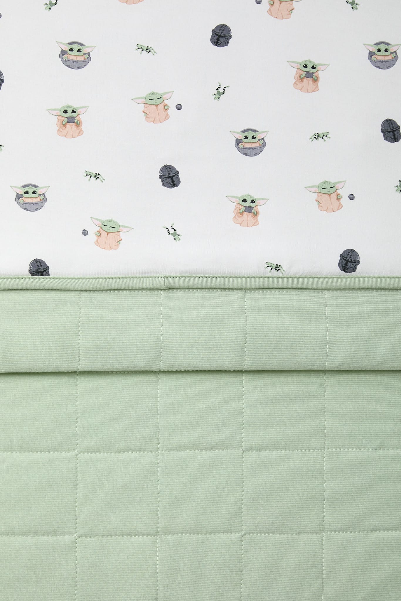 Close up of the light green quilted backing and the smooth printed top layer shown on the Toddler Blanket in Grogu™ 1.0