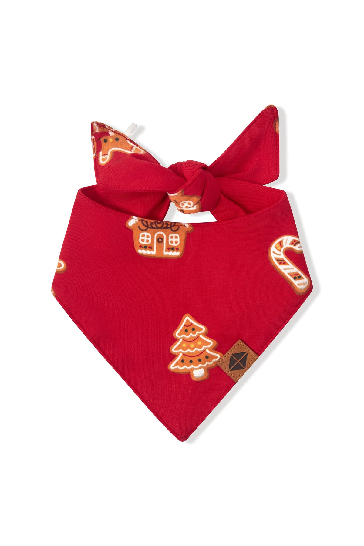 A red pet bandana featuring a festive Christmas print with gingerbread houses, candy canes, and a Christmas tree, tied in a knot at the top.