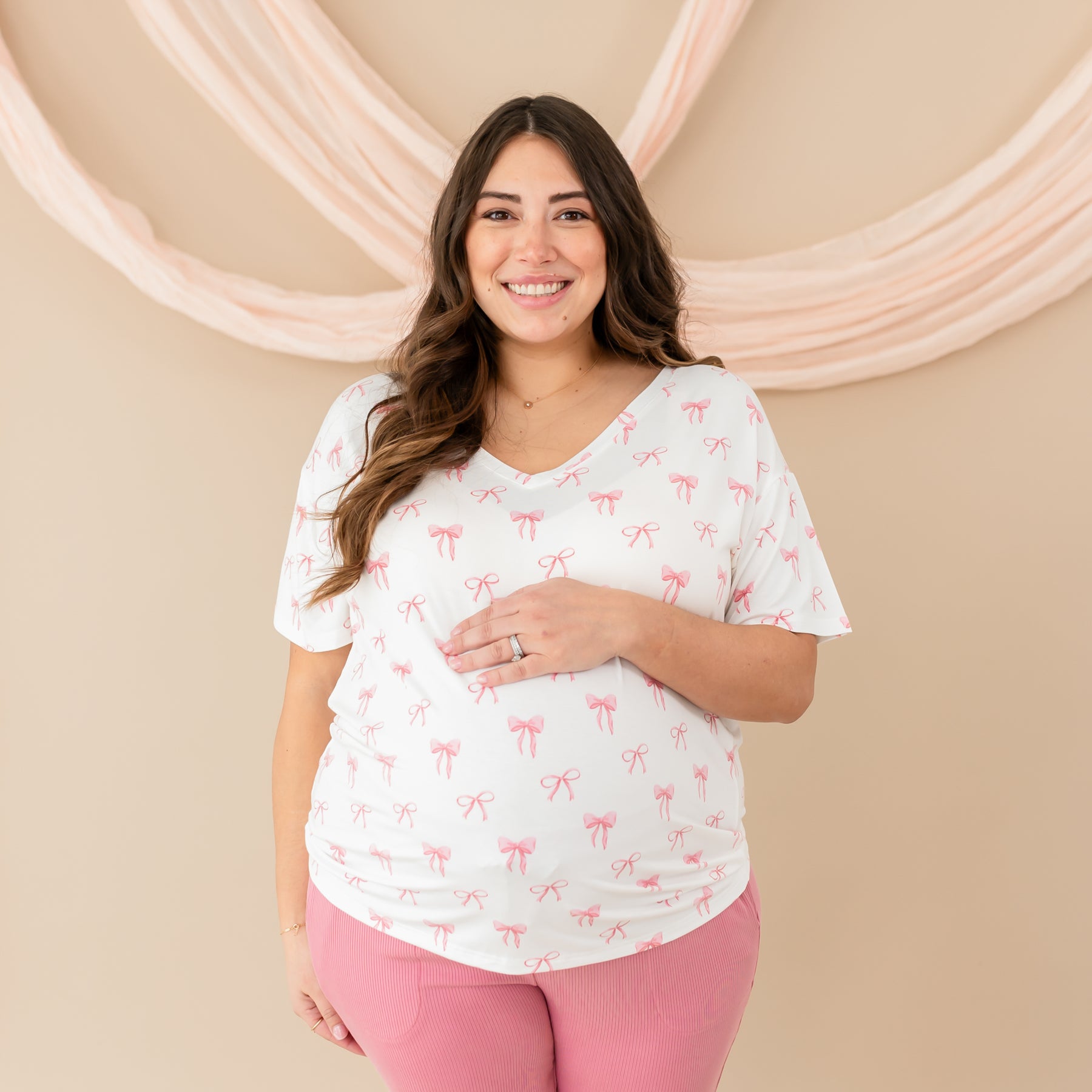 Pregnant woman smiling and wearing Women’s Relaxed Fit V-Neck in Bow with Apple Blossom Ribbed Jogger Pants. 