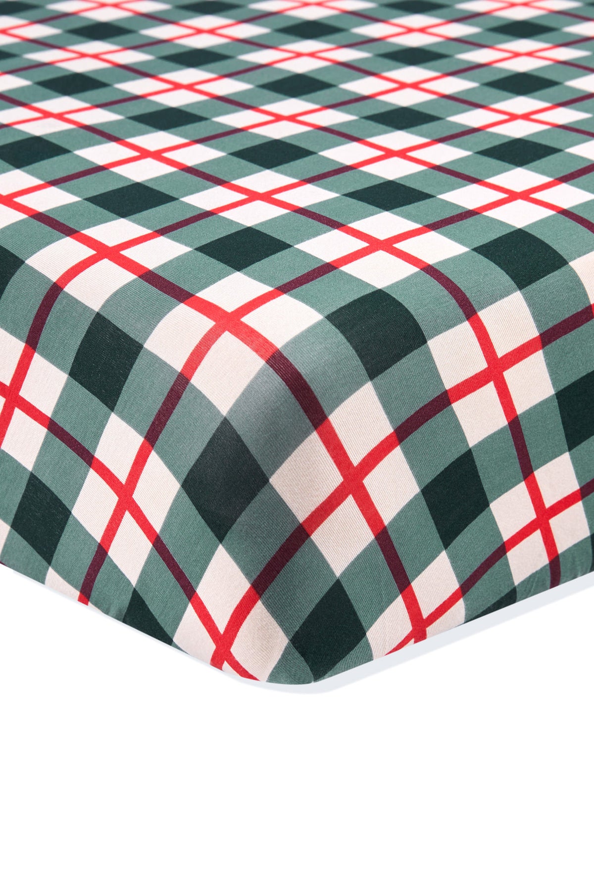 A close-up of a plaid fabric surface, likely a fitted sheet or blanket, featuring a green, white, and red tartan pattern on a white background.