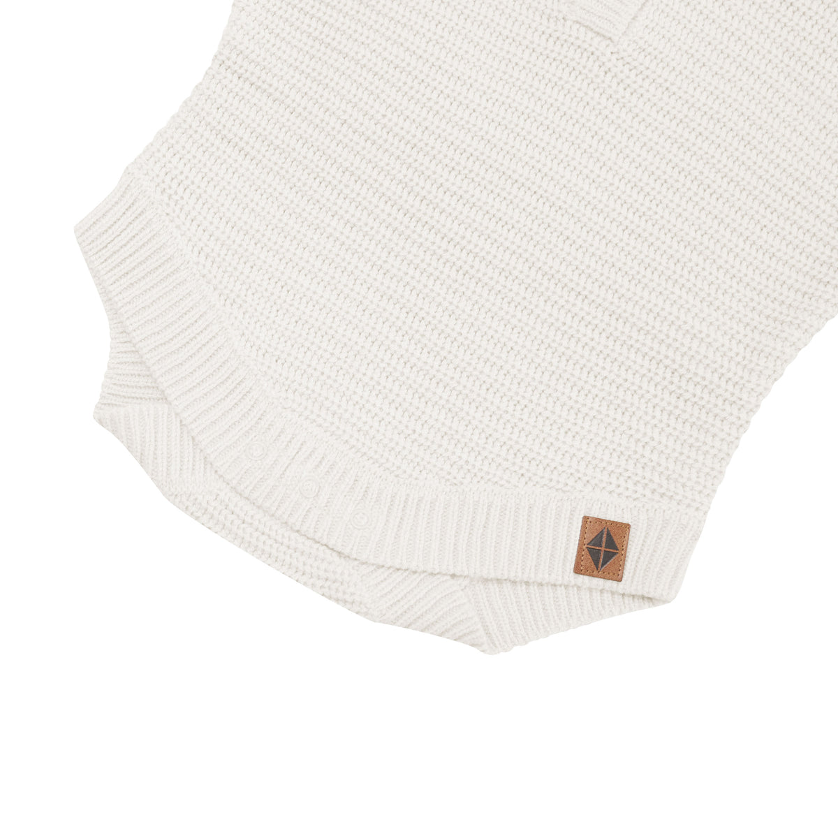 Snap closure shown on the Chunky Knit Romper in Oat with the Kyte Baby vegan leather tag visible
