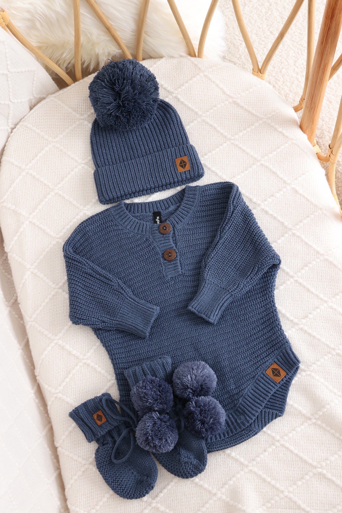 Chunky knit pom beanie, chunky knit romper and knit booties in oxford laid in a crib