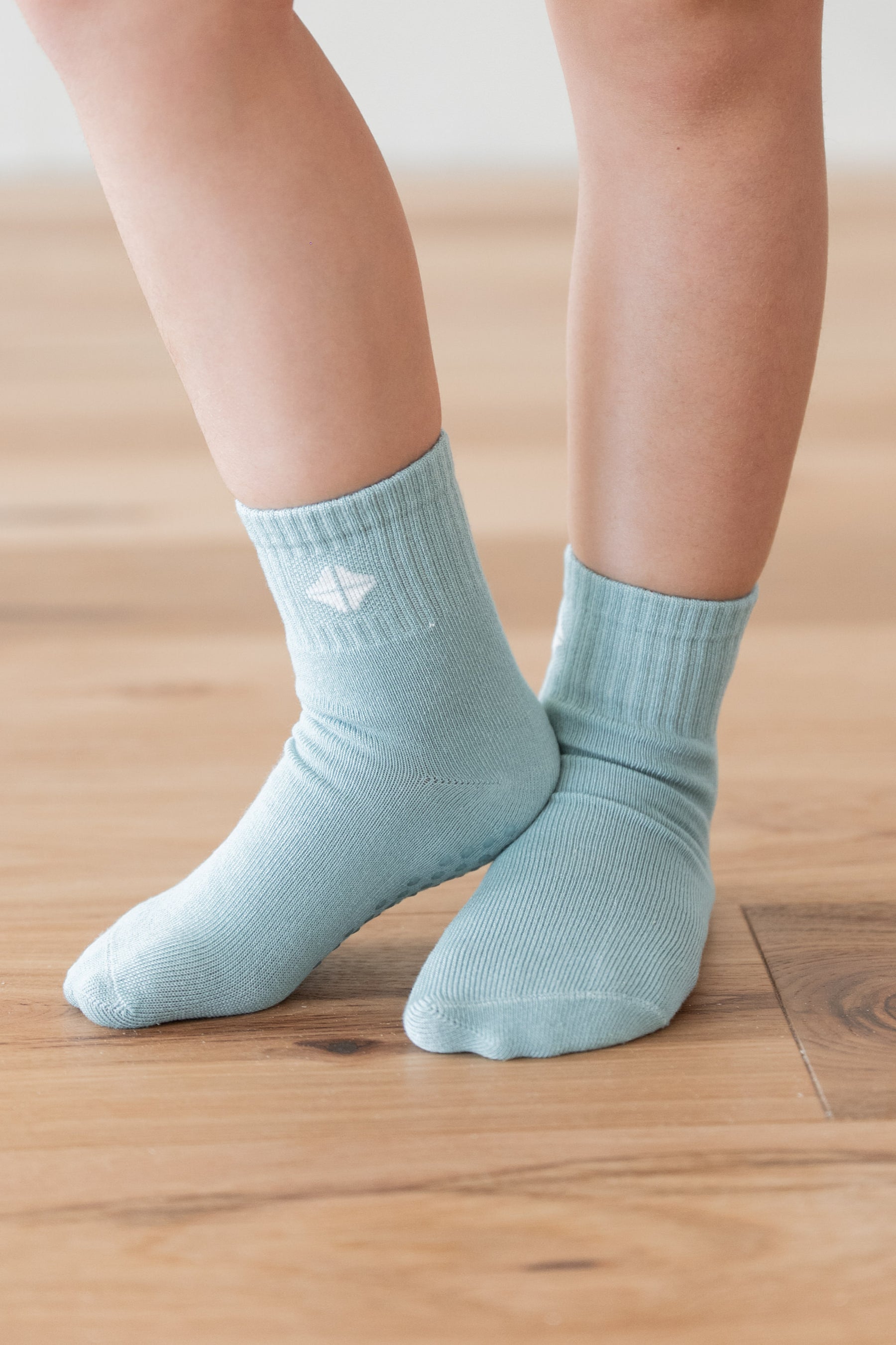A close-up of a person's feet wearing light sage green ribbed ankle socks on a light wood floor.