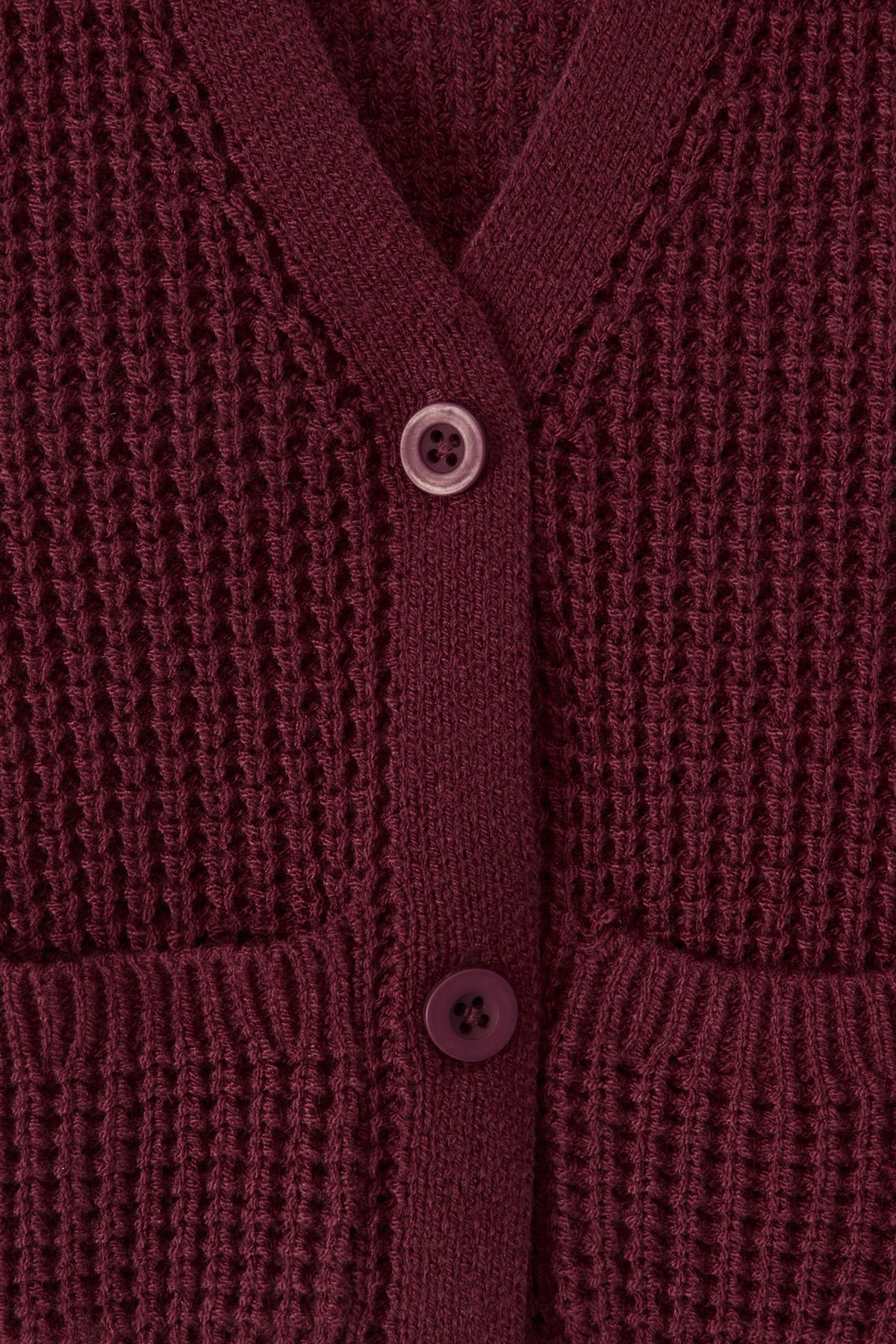 Close-up of a textured knit cardigan in a burgundy color, featuring a waffle-weave pattern, ribbed trim, and two white buttons.