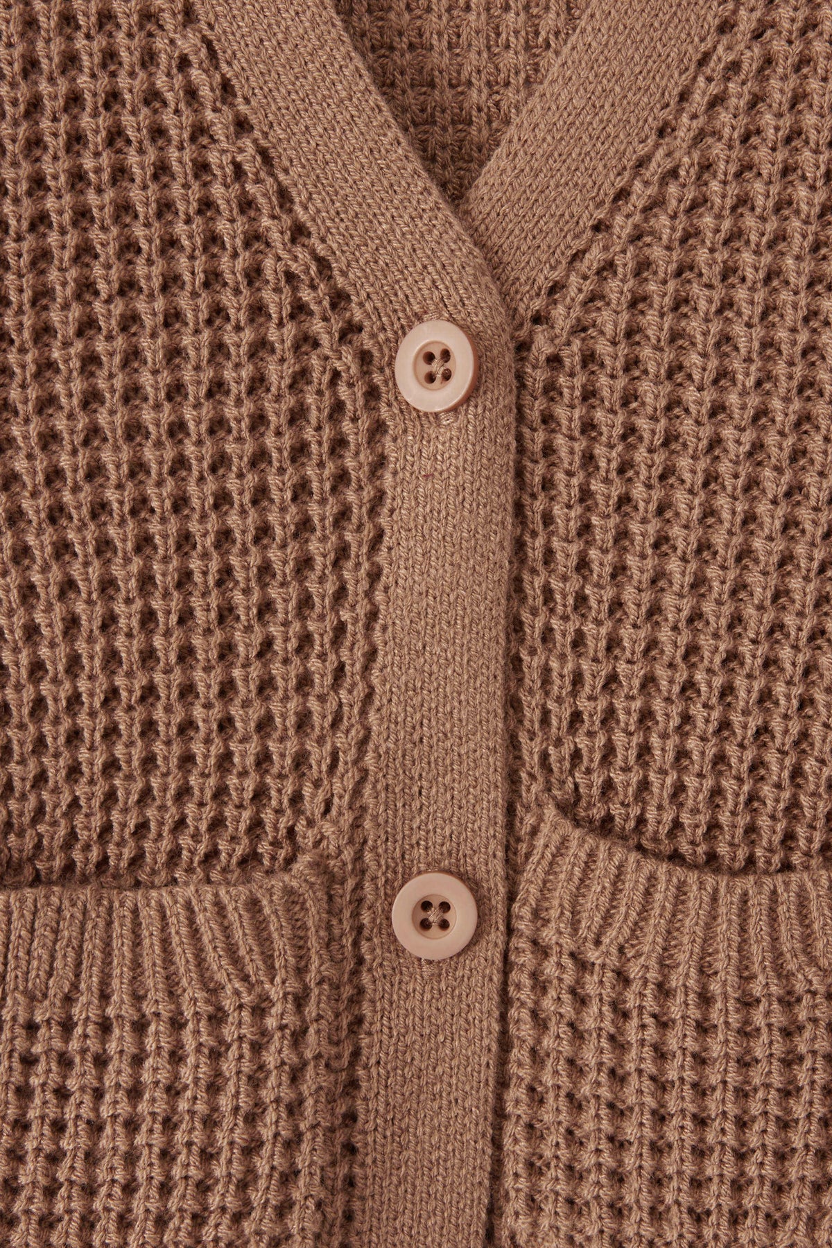 Close-up of a textured knit cardigan in latte color, featuring a waffle-weave pattern, ribbed trim, and two white buttons.