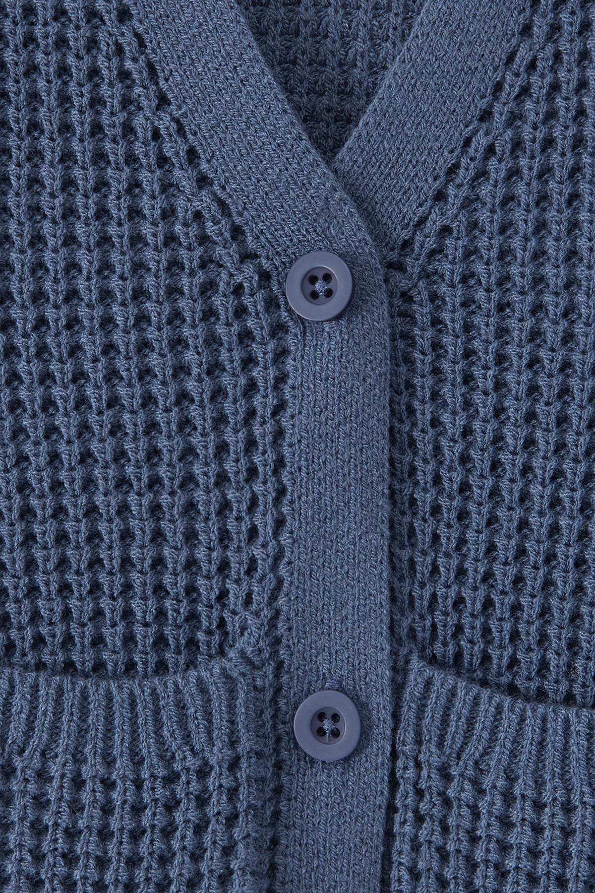 Close-up of a textured knit cardigan in a blue color, featuring a waffle-weave pattern, ribbed trim, and two white buttons.