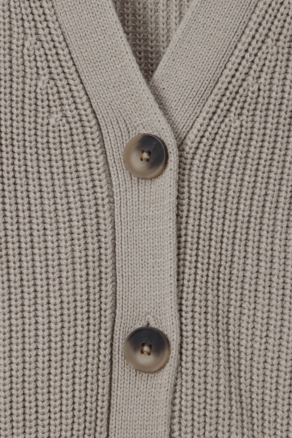 Close-up of a ribbed knit cardigan sweater in a light taupe-beige color, featuring two dark brown buttons on the front.