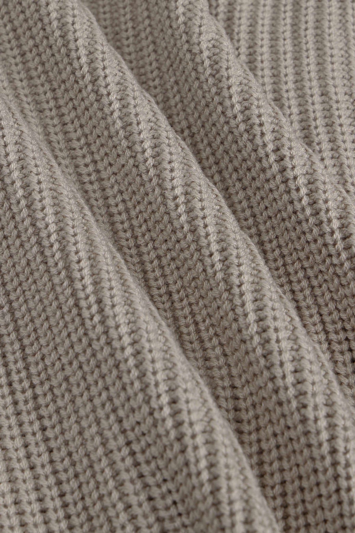 Close-up of a ribbed knit fabric in a warm taupe-beige color, showing the detailed texture and folds of the material.