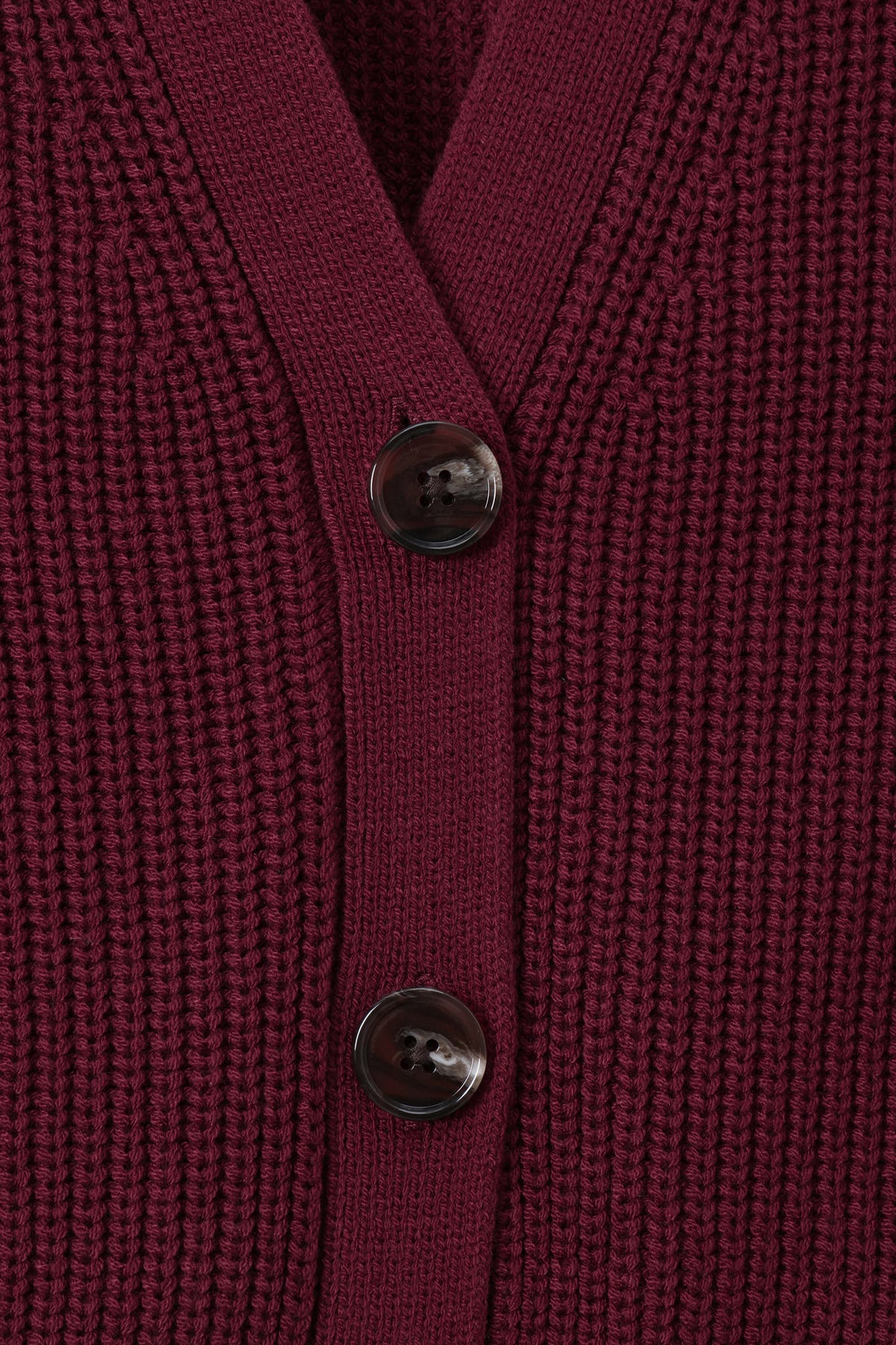 Close-up of a ribbed knit cardigan in deep burgundy with two dark buttons, showing the texture and neckline detail.