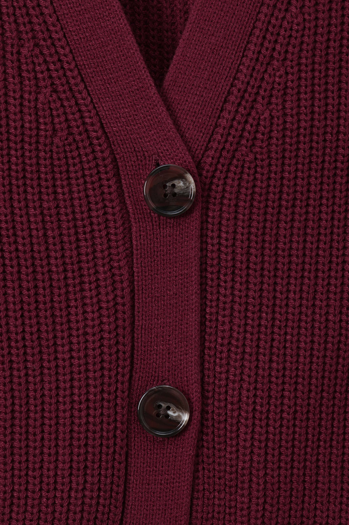 Close-up of a ribbed knit cardigan in deep burgundy with two dark buttons, showing the texture and neckline detail.