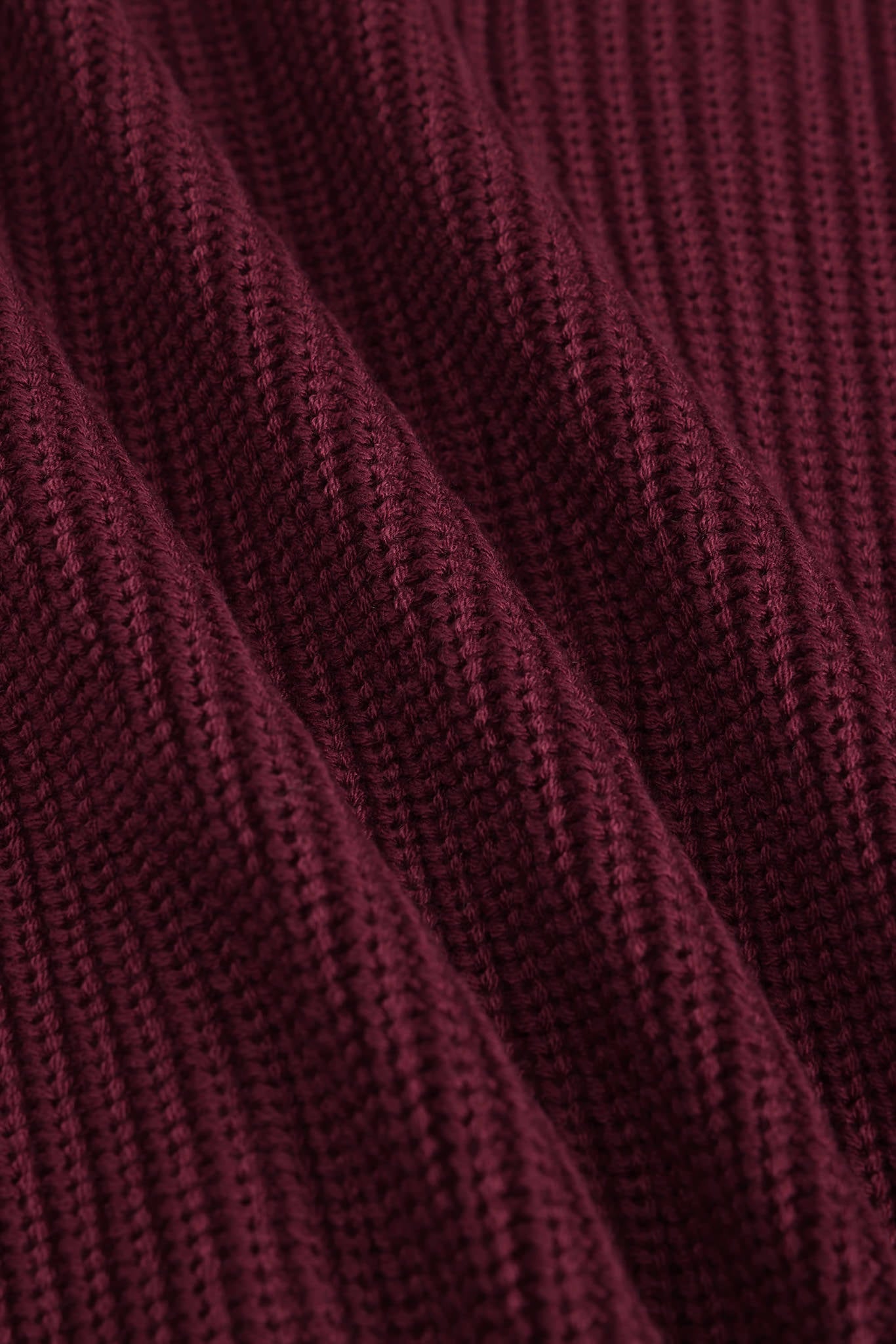 Close-up of a ribbed knit fabric in a deep burgundy or maroon color, showing the detailed texture and folds of the material.