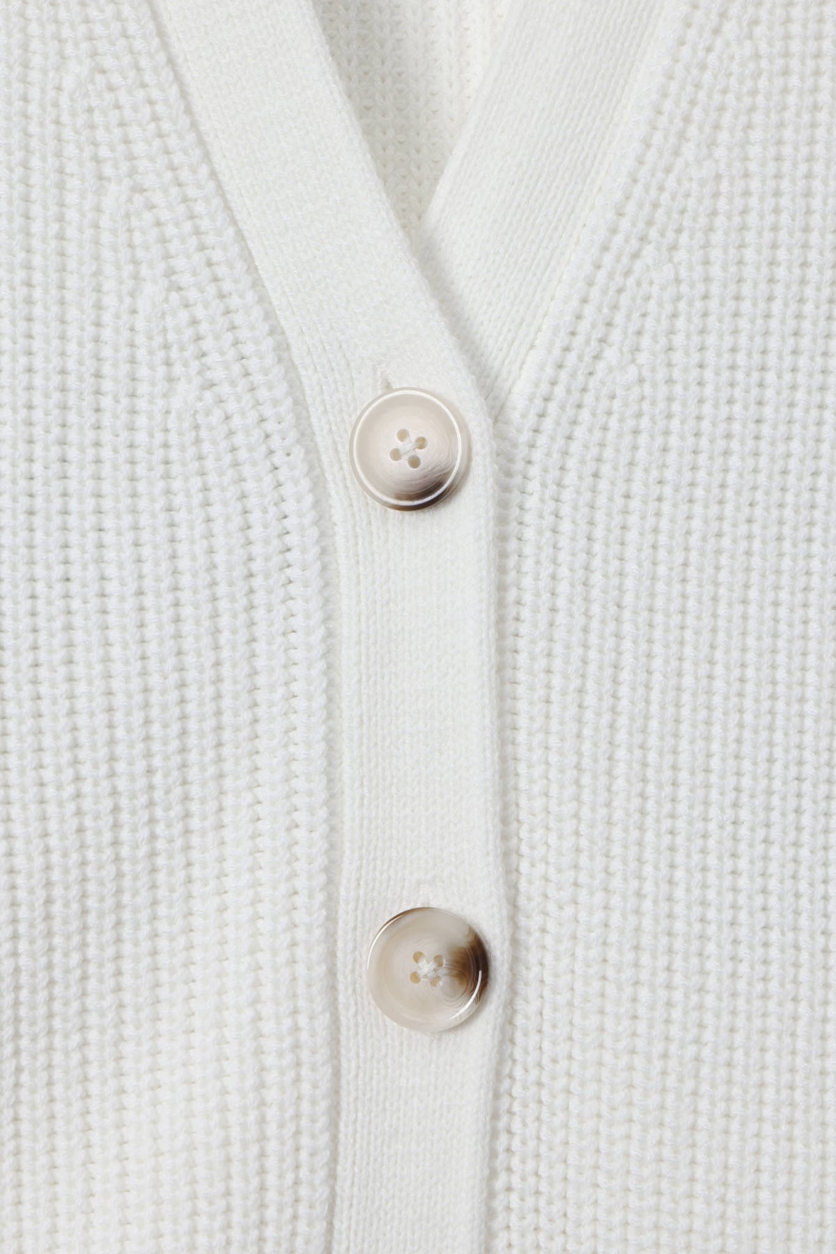 Close-up of a white ribbed knit cardigan with two beige buttons on a clean white background.