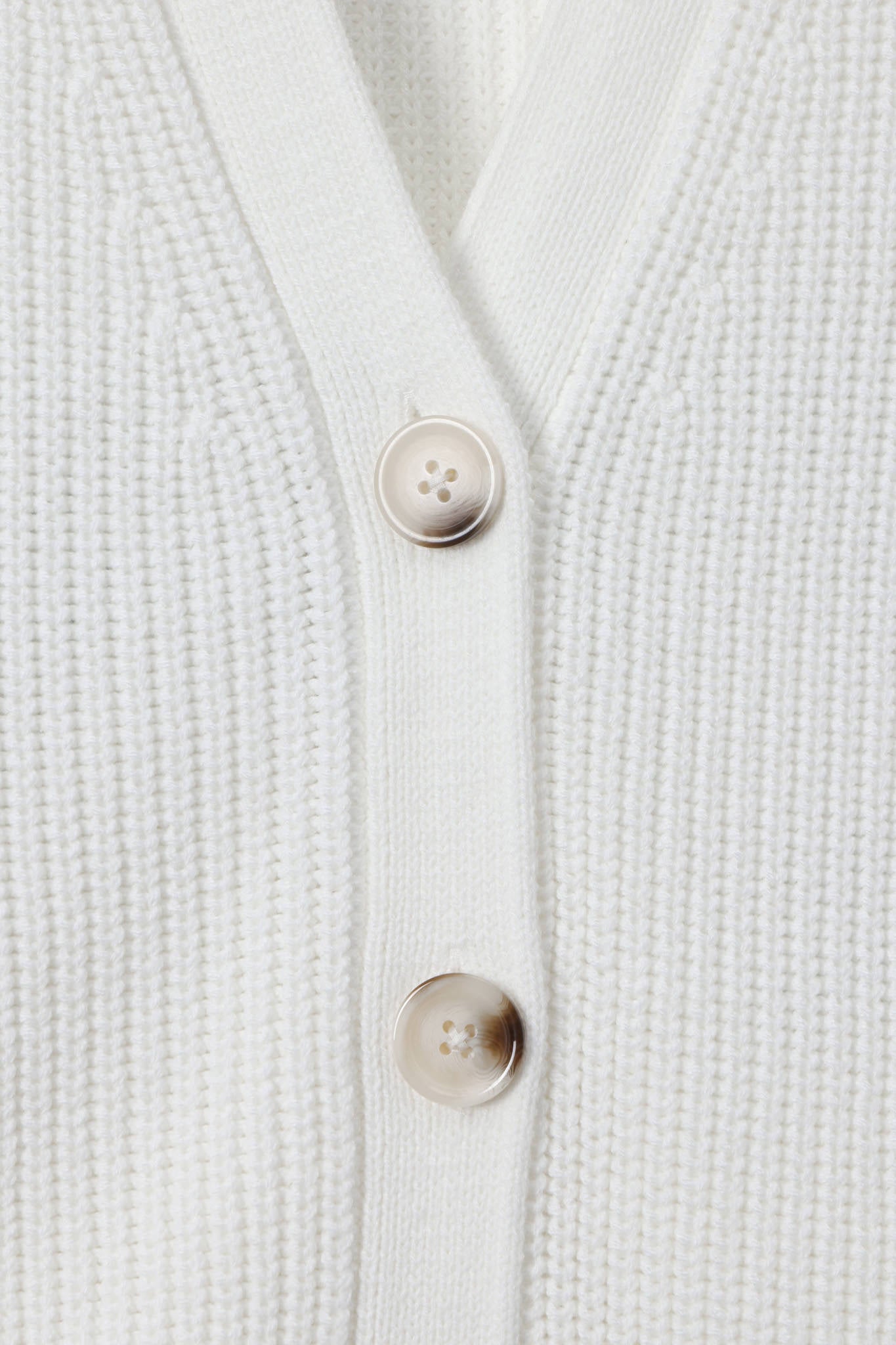 Close-up of a white ribbed knit cardigan with two beige buttons on a clean white background.