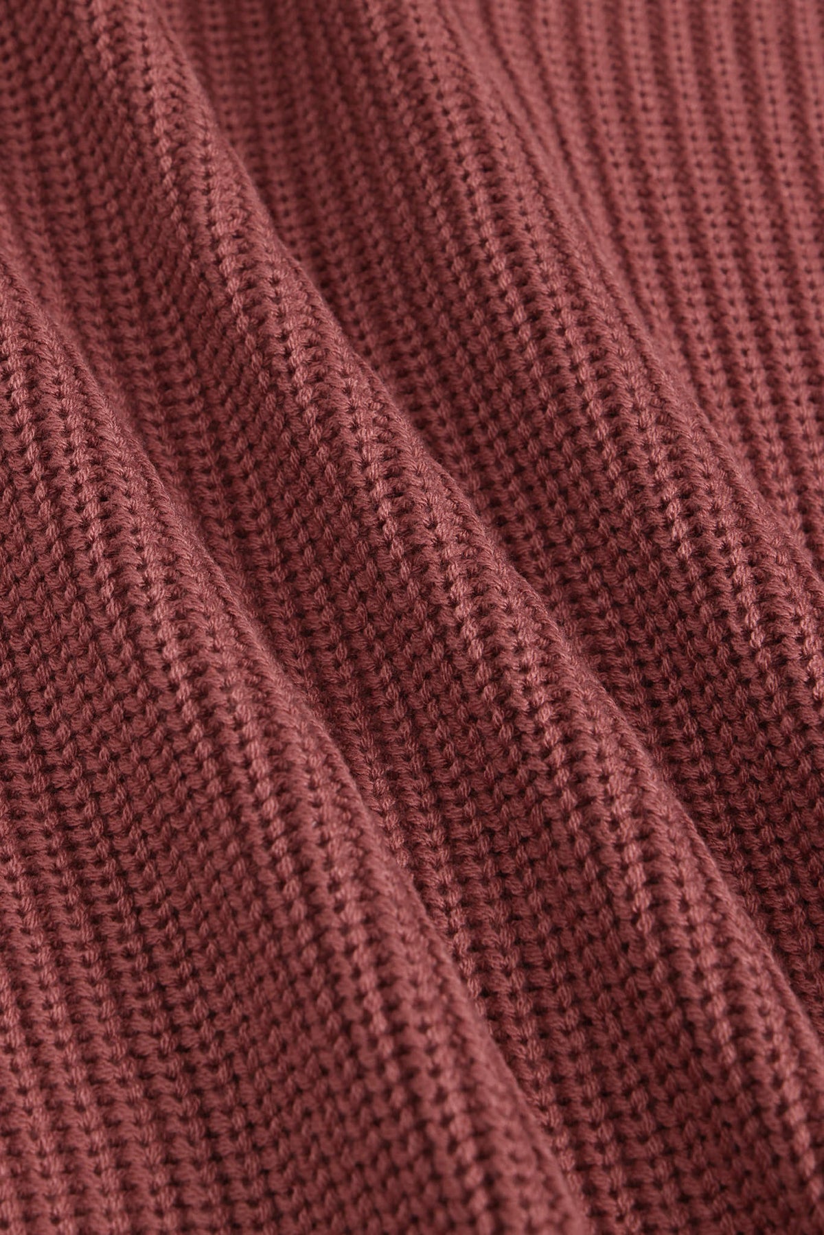 Close-up of a ribbed knit fabric in a dusty rose or mauve color, showing the detailed texture and folds of the material.
