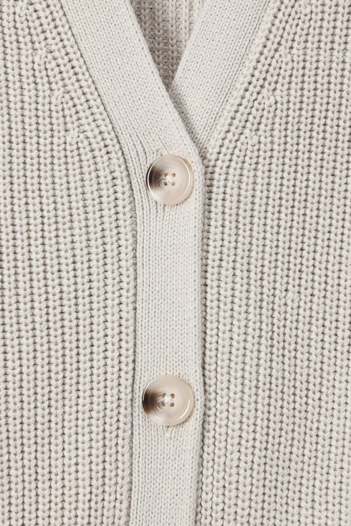 Close-up of a cream-colored ribbed knit cardigan sweater showing the button placket with two light beige buttons.