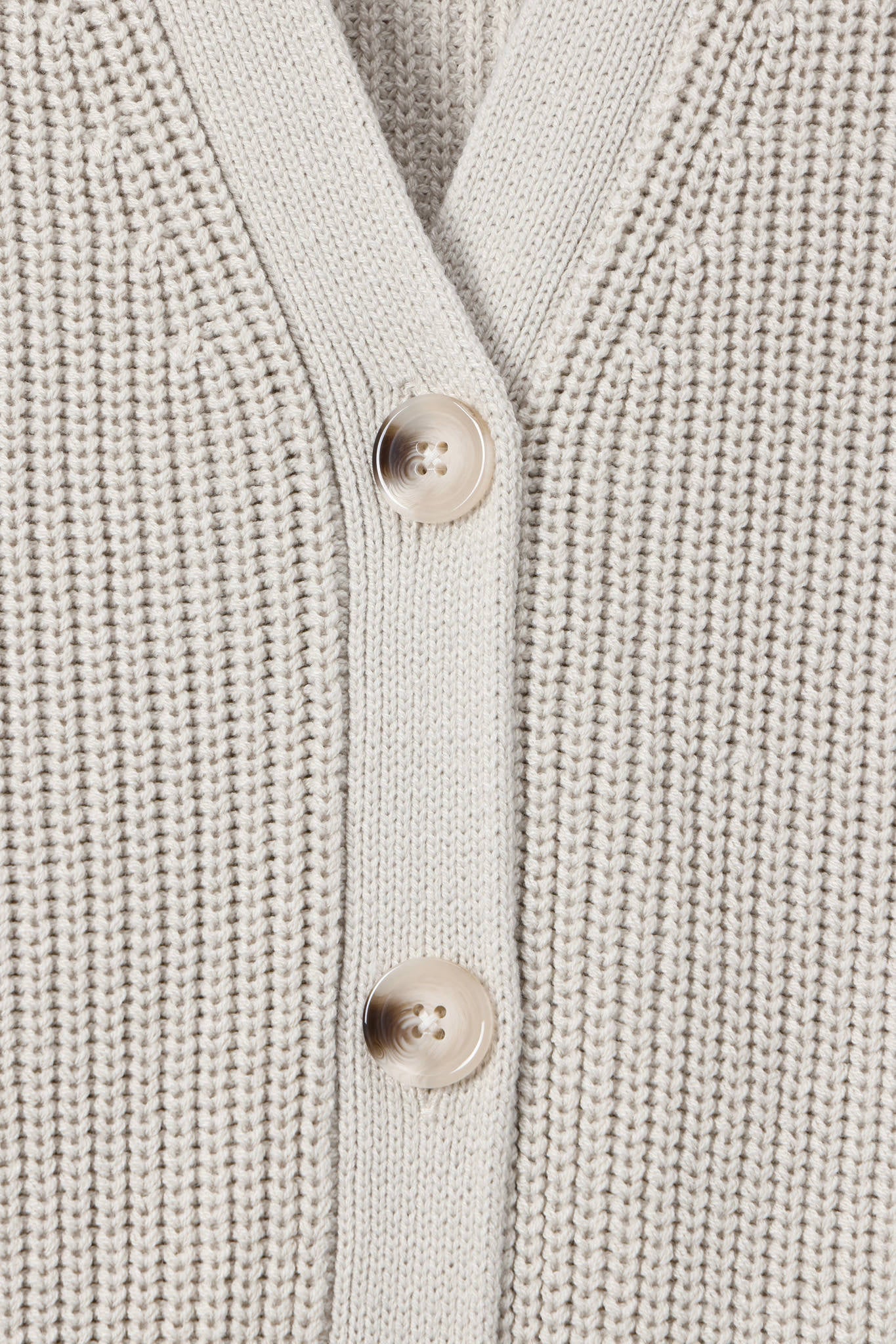 Close-up of a cream-colored ribbed knit cardigan sweater showing the button placket with two light beige buttons.