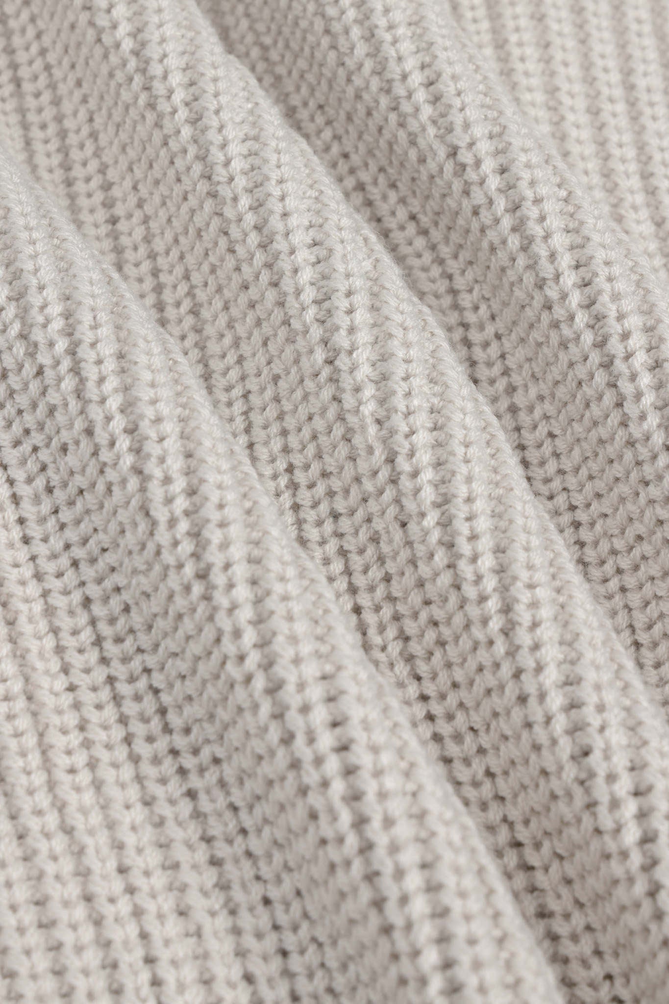 Close-up of a ribbed knit fabric in a light oatmeal beige color, showing the detailed texture and folds of the yarn.