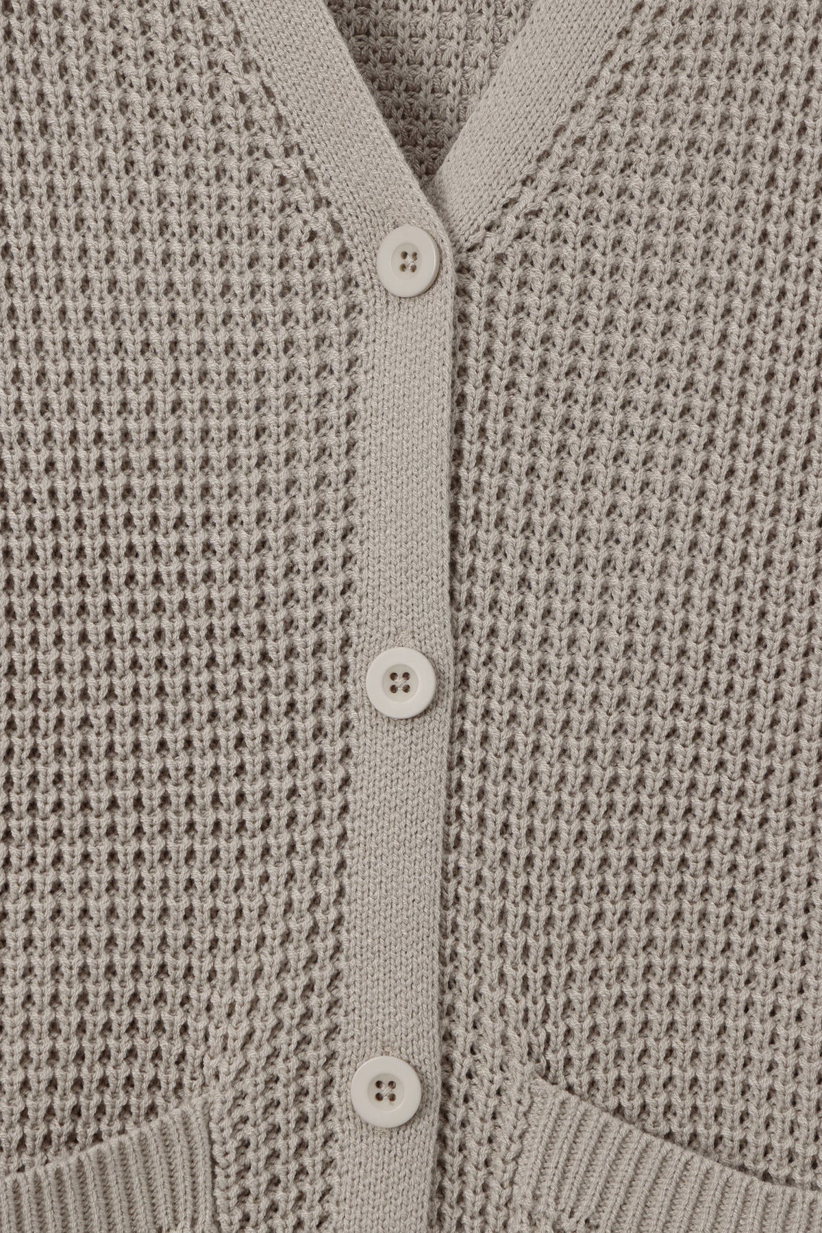 Close-up of a light taupe knit cardigan sweater showing the waffle-knit texture, V-neckline, and white buttons.