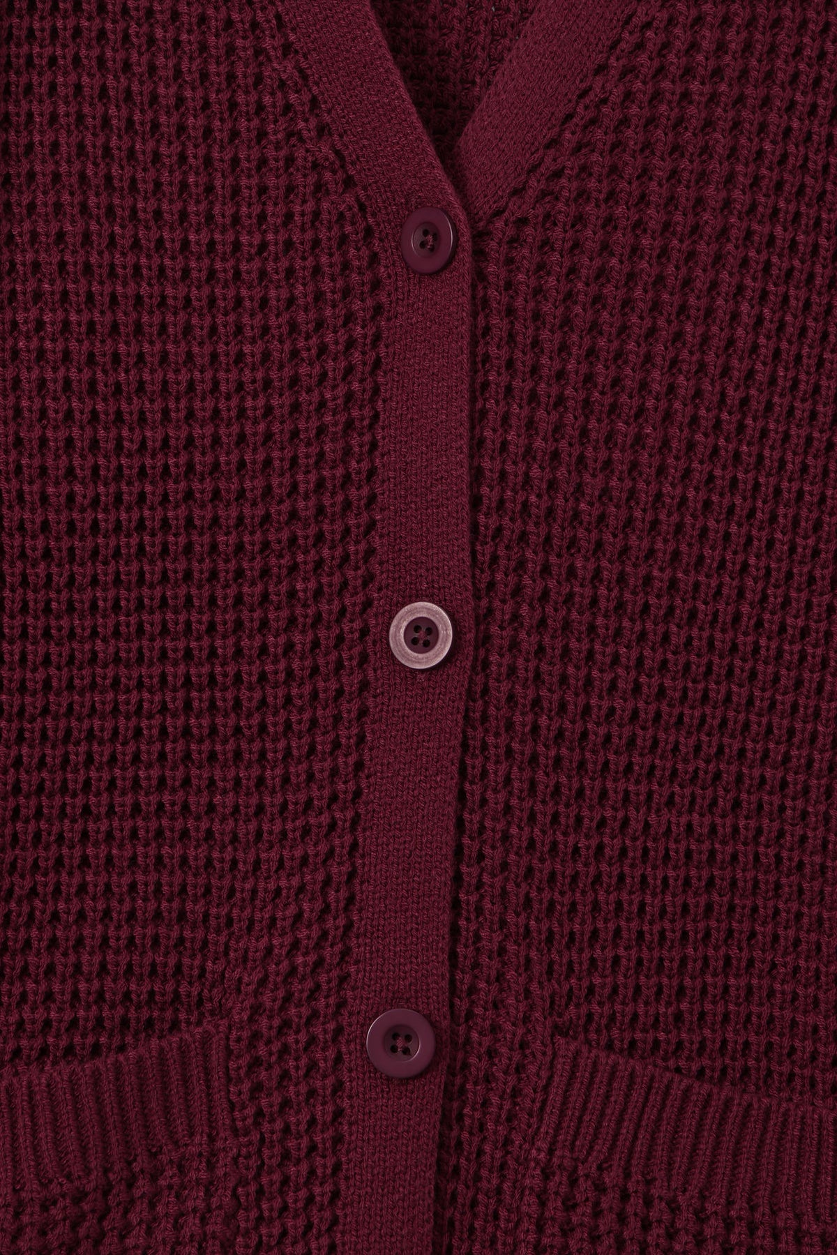 Close-up of a textured knit cardigan in deep burgundy with matching buttons, showing the ribbed collar, button placket, and pocket openings.