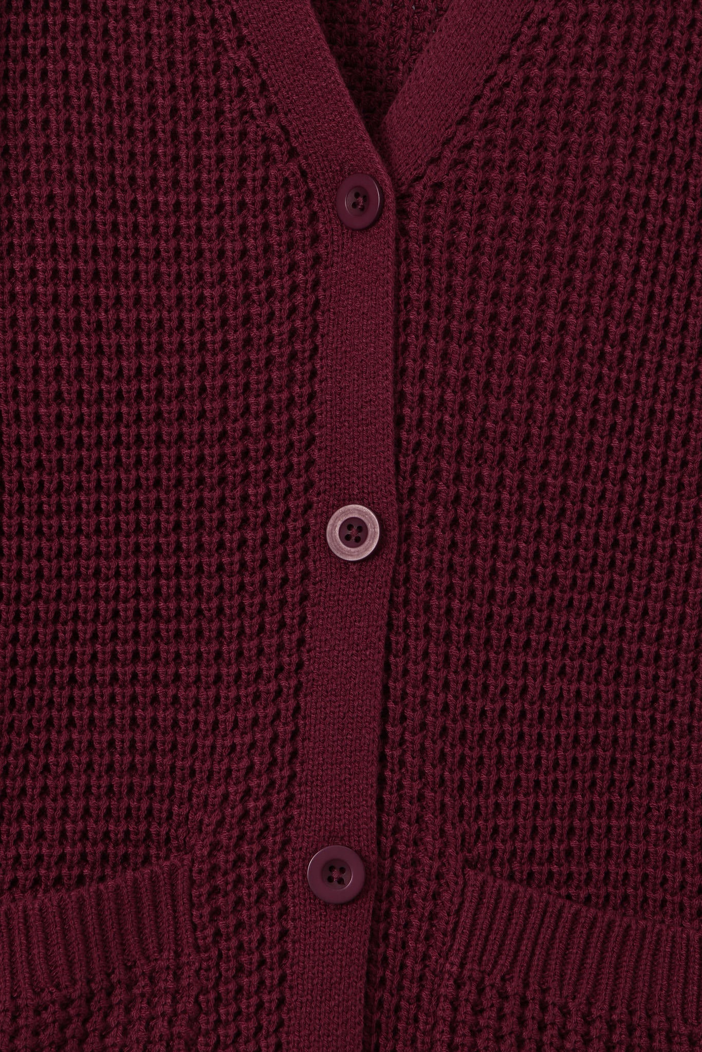 Close-up of a textured knit cardigan in deep burgundy with matching buttons, showing the ribbed collar, button placket, and pocket openings.