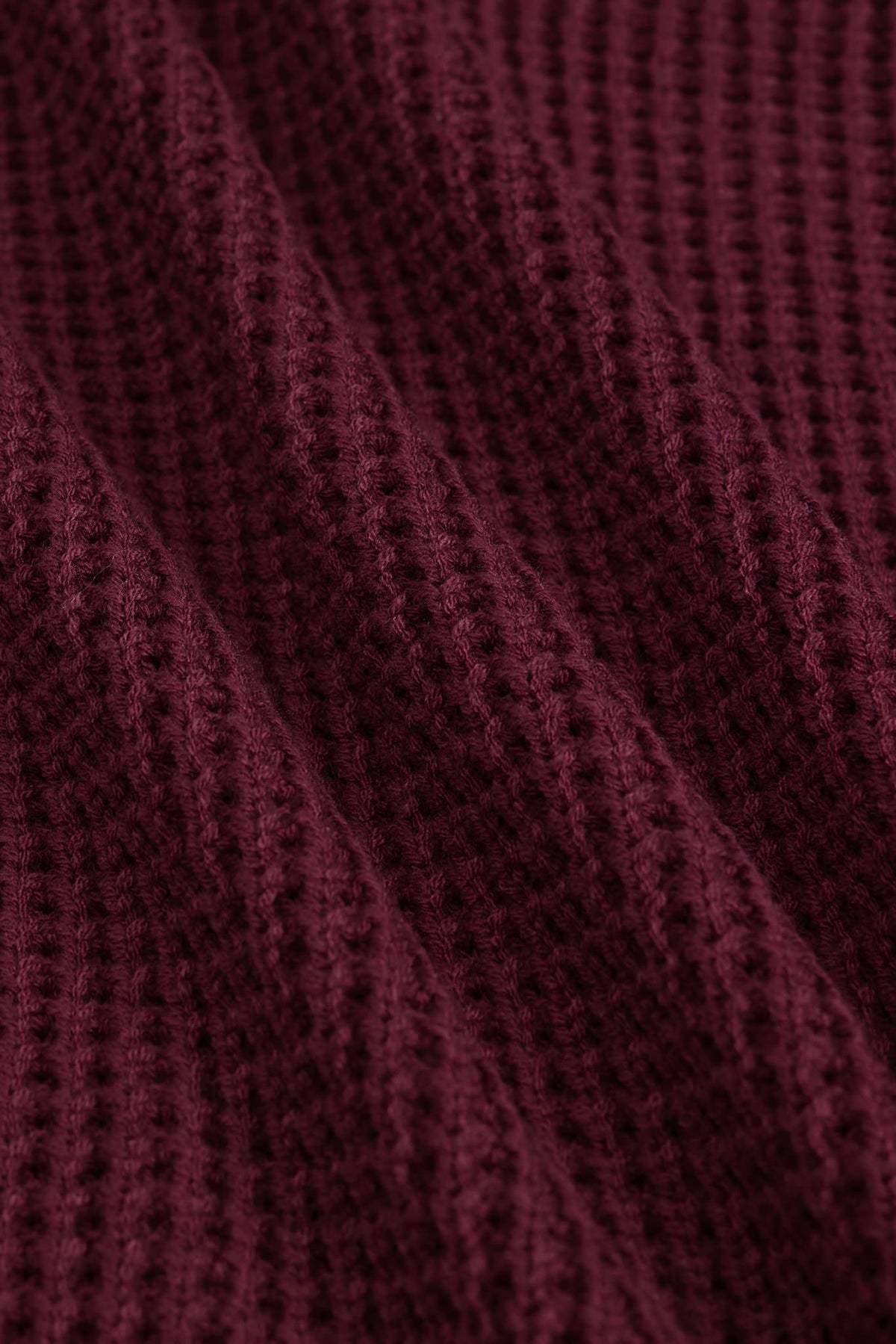 A close-up of a textured knit fabric in a deep burgundy or maroon color, showing the detailed waffle-knit pattern and soft folds.