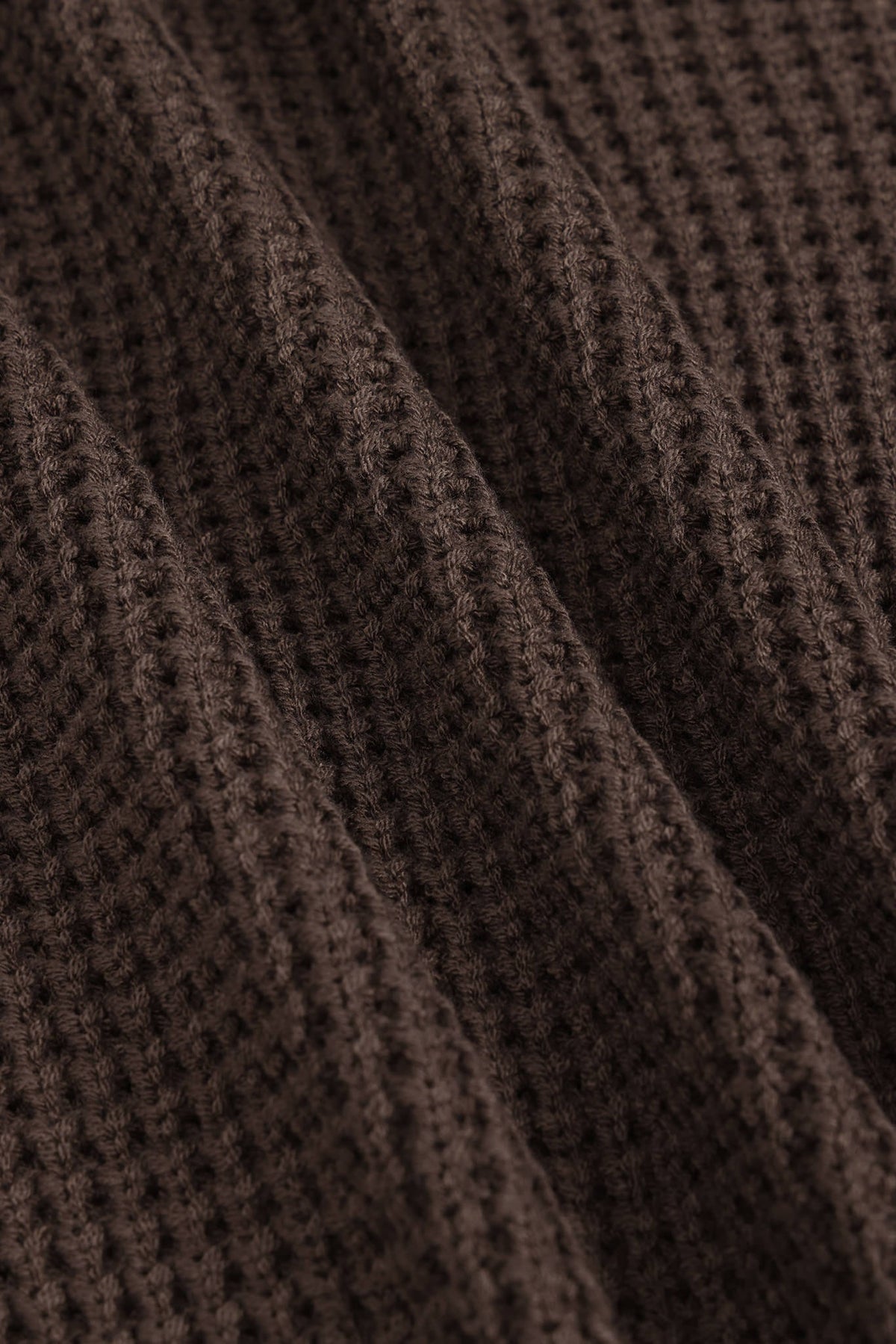 Close-up of a dark brown waffle-knit fabric with soft diagonal folds showing the textured knit pattern.