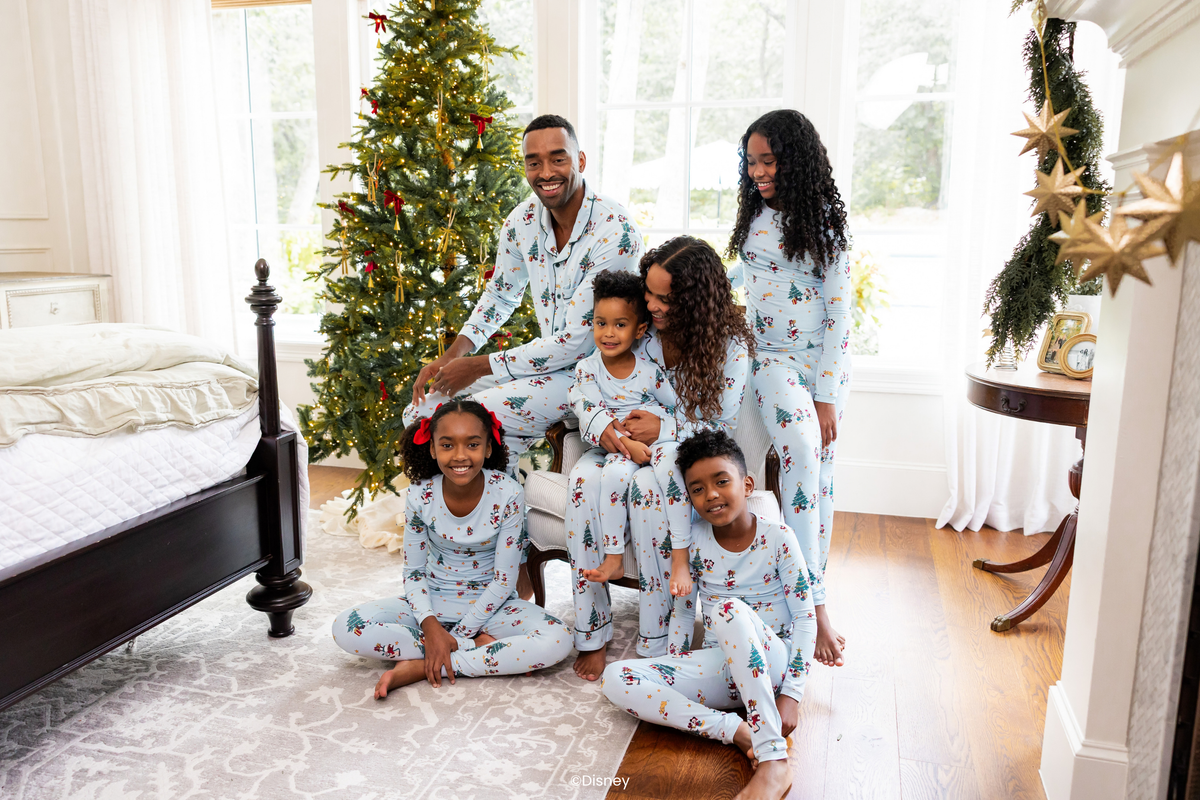 family of six wearing blue mickey and friends pajamas in a festive bedroom with christmas tree in the background