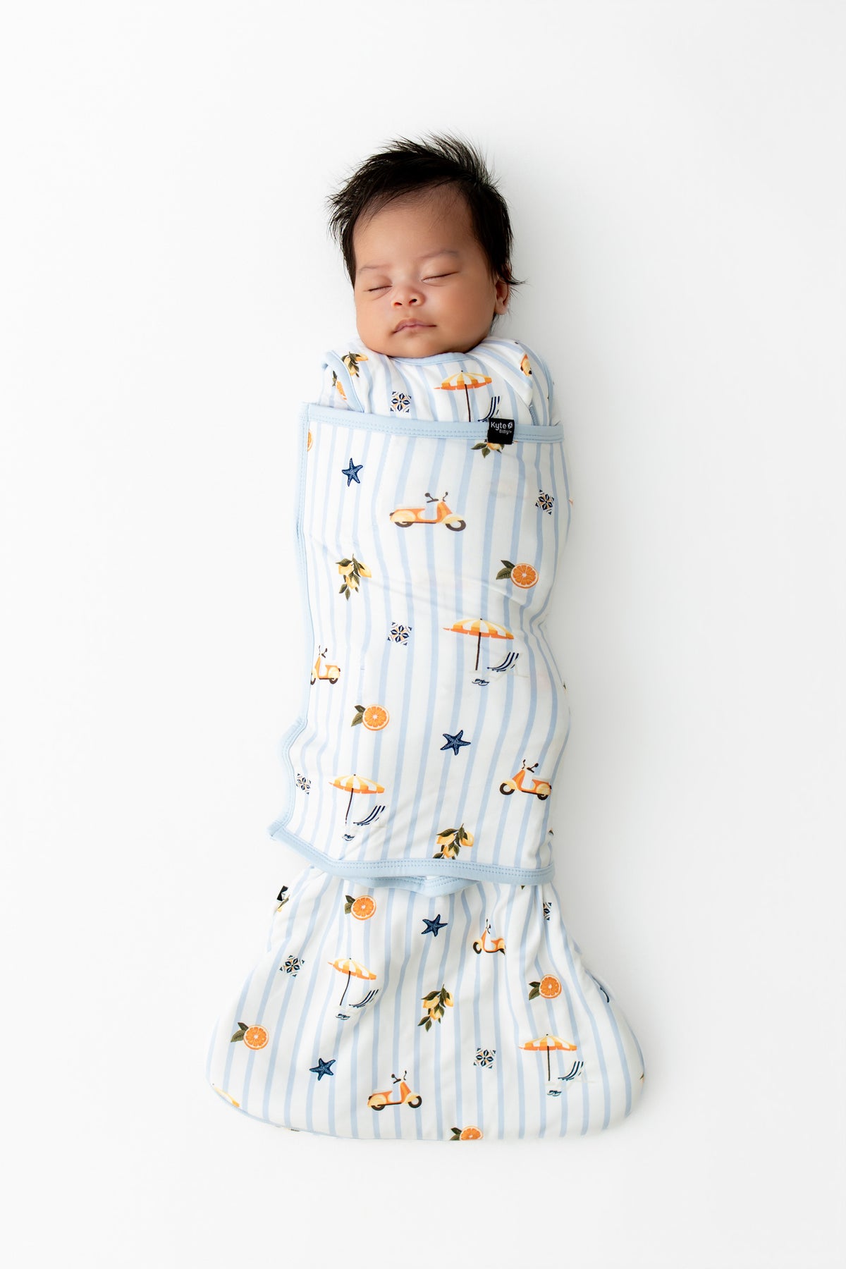 Sleeping newborn swaddled in the Sleep Bag Swaddler in Amalfi Coast 1.0 on white background