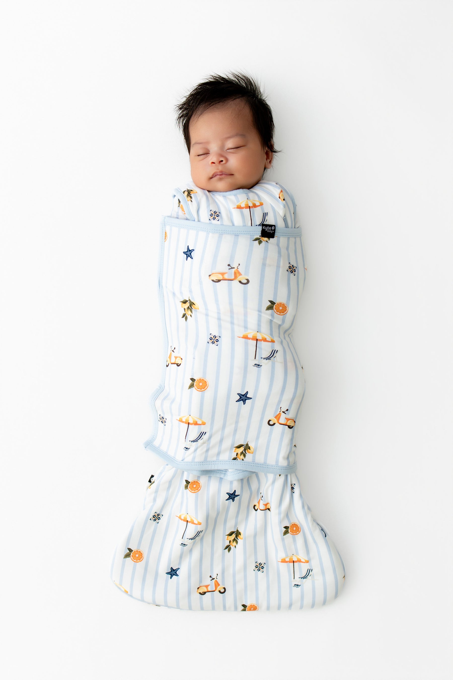 Sleeping newborn swaddled in the Sleep Bag Swaddler in Amalfi Coast 1.0 on white background