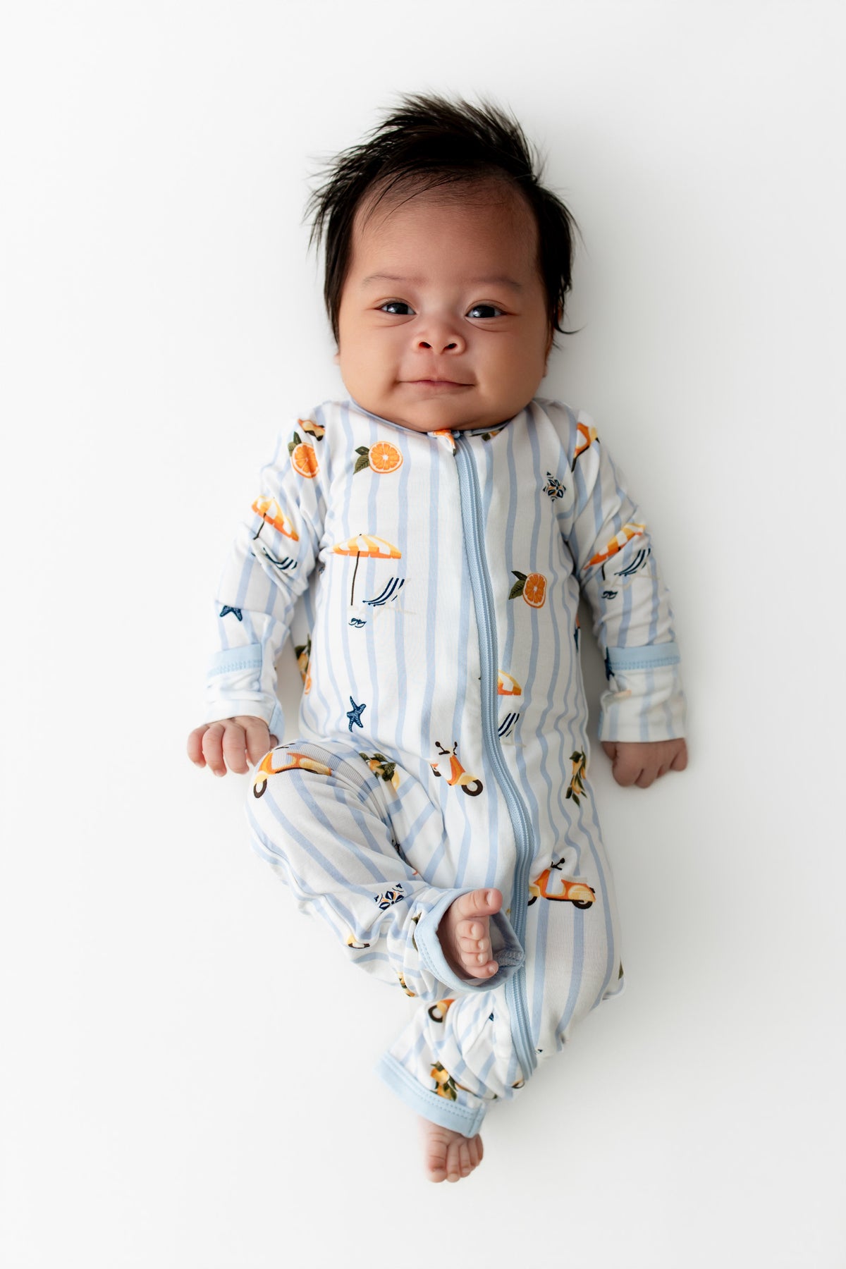 Newborn laying on a white surface wearing the Zippered Romper in Amalfi Coast