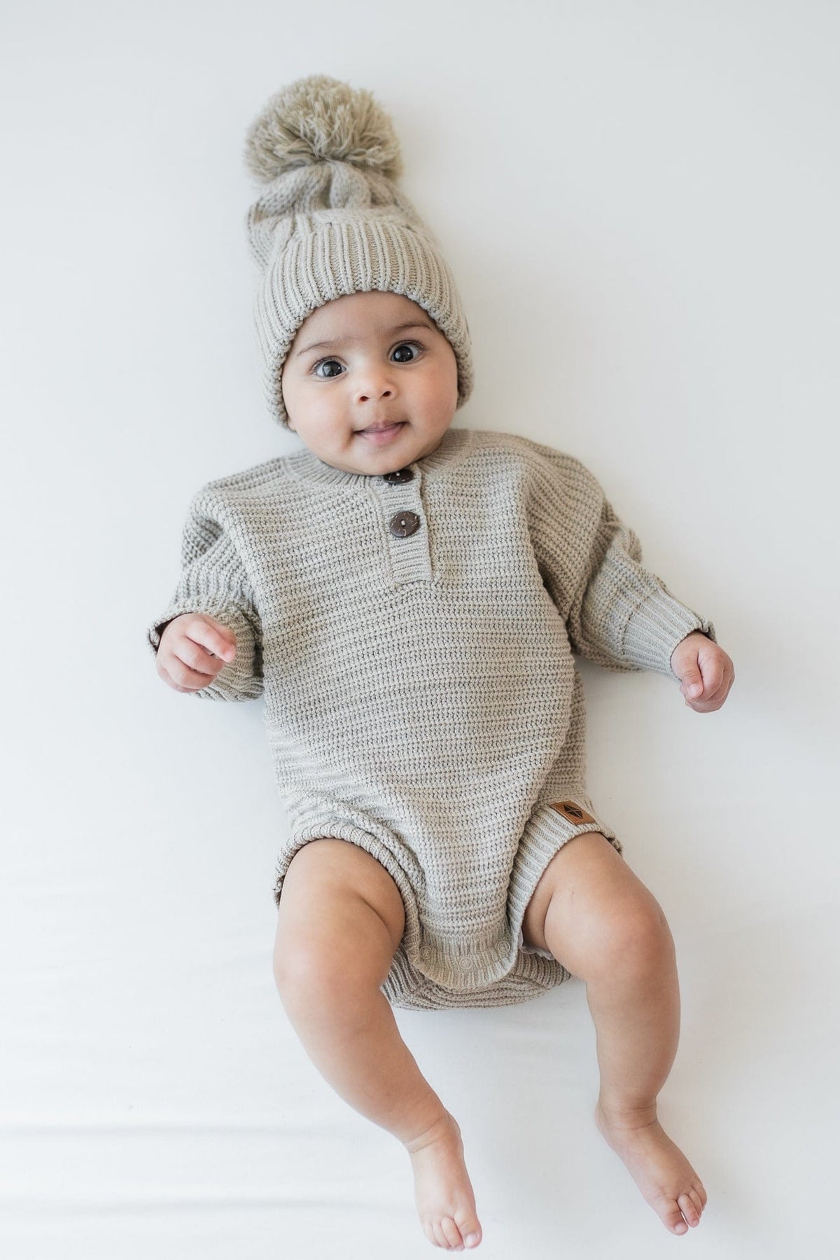 Infant wearing the Chunky Cable Knit Beanie in Almond and matching chunky knit romper