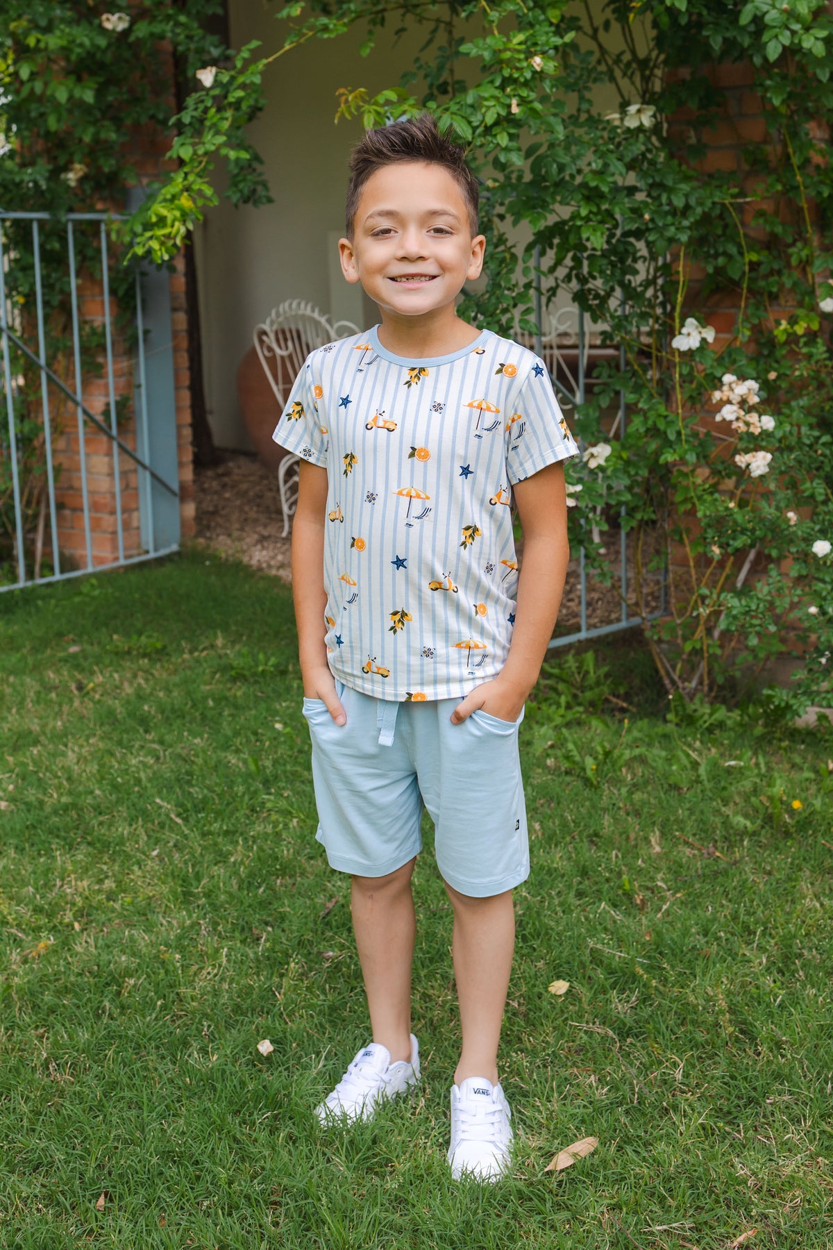 Young boy wearing a tshirt with stripes and amalfi coast inspired icons and blue shorts in an outdoor setting