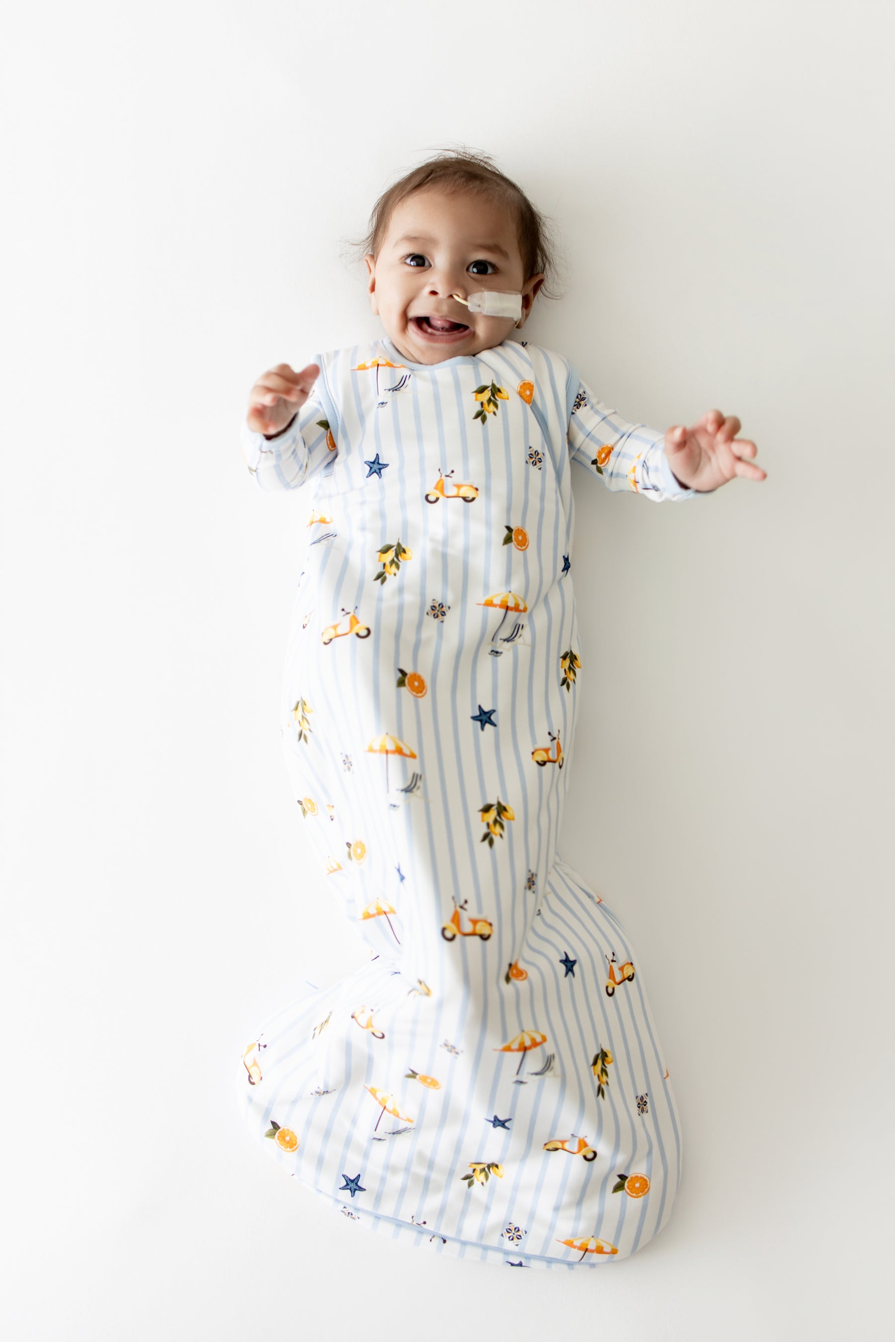 Infant laying on a white surface wearing the Sleep Bag in Amalfi Coast 1.0 with matching romper on underneath