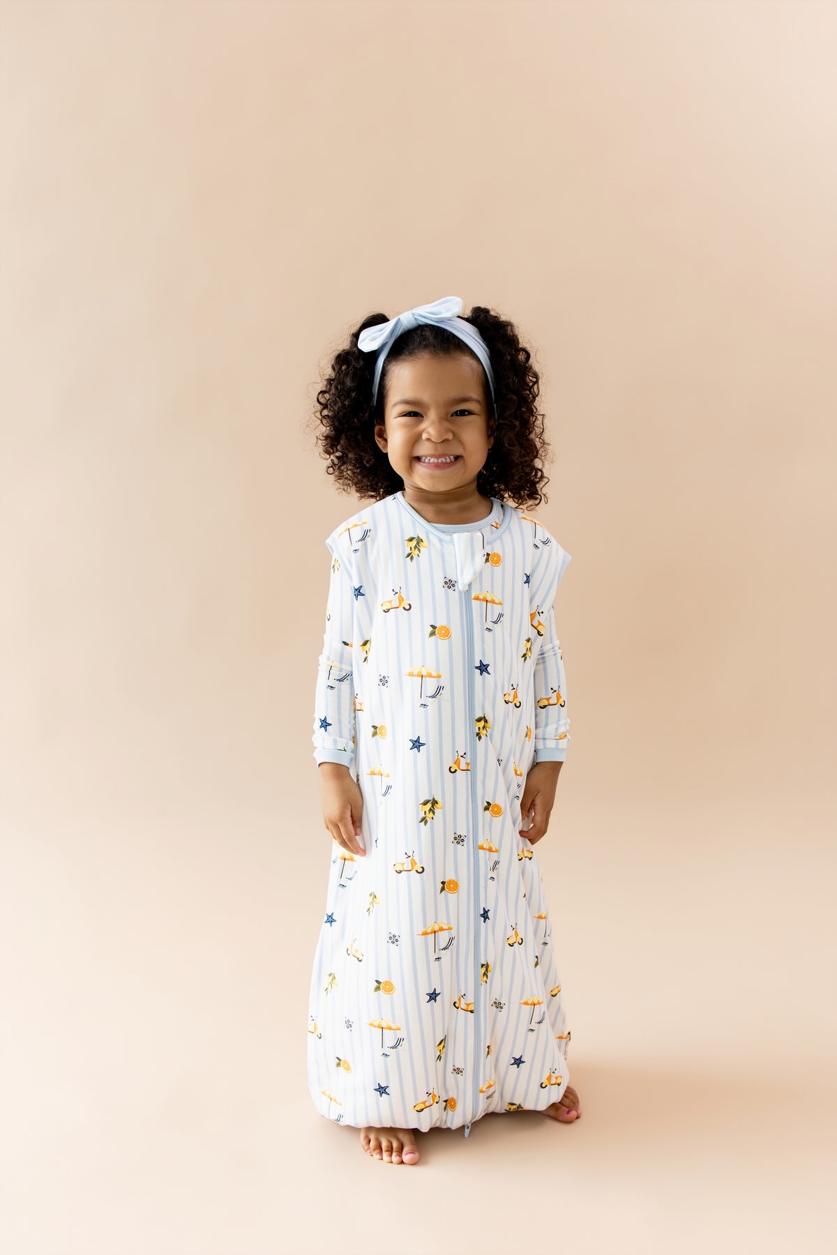Smiling girl wearing the Sleep Bag Walker in Amalfi Coast 1.0 with light blue bow