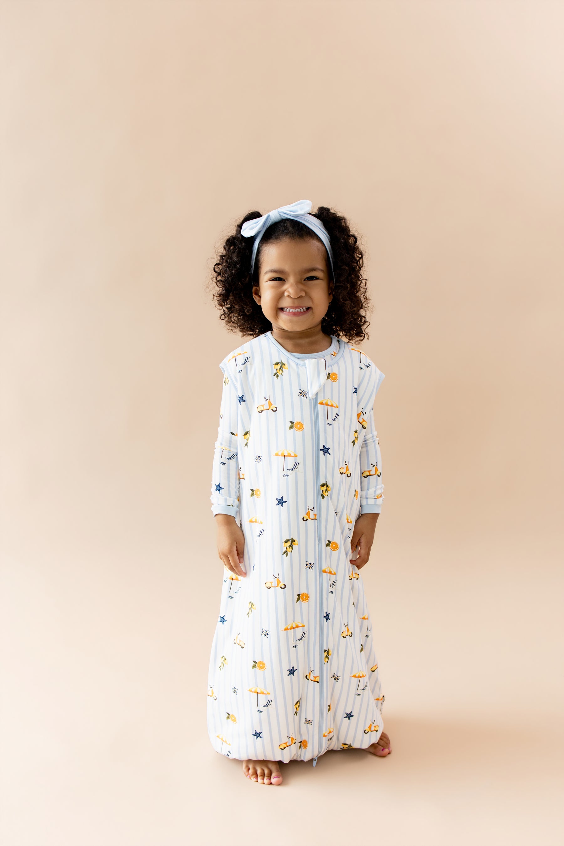 Smiling girl wearing the Sleep Bag Walker in Amalfi Coast 1.0 with light blue bow