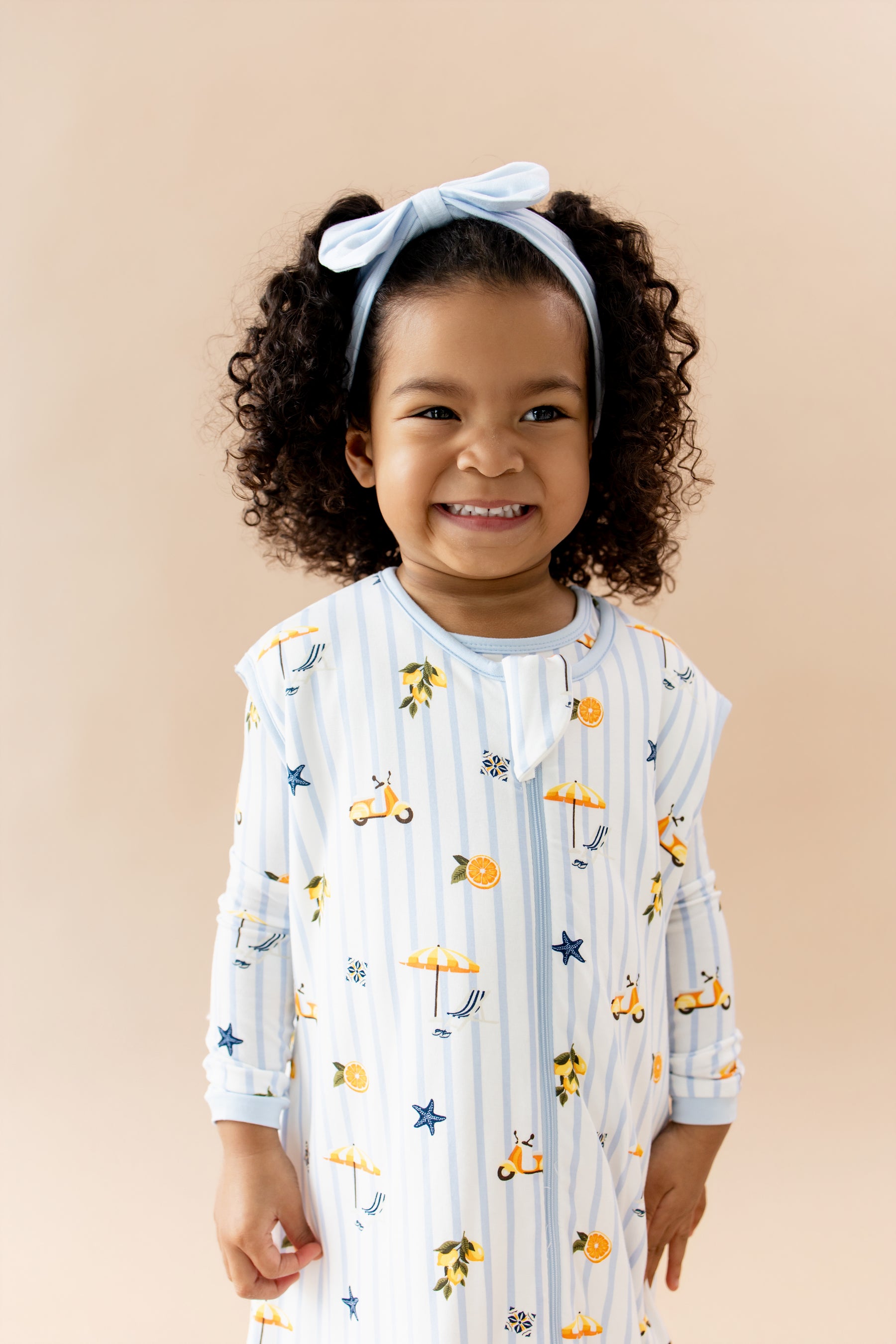 Smiling girl wearing the Sleep Bag Walker in Amalfi Coast 1.0 with matching long sleeve pajamas on underneath