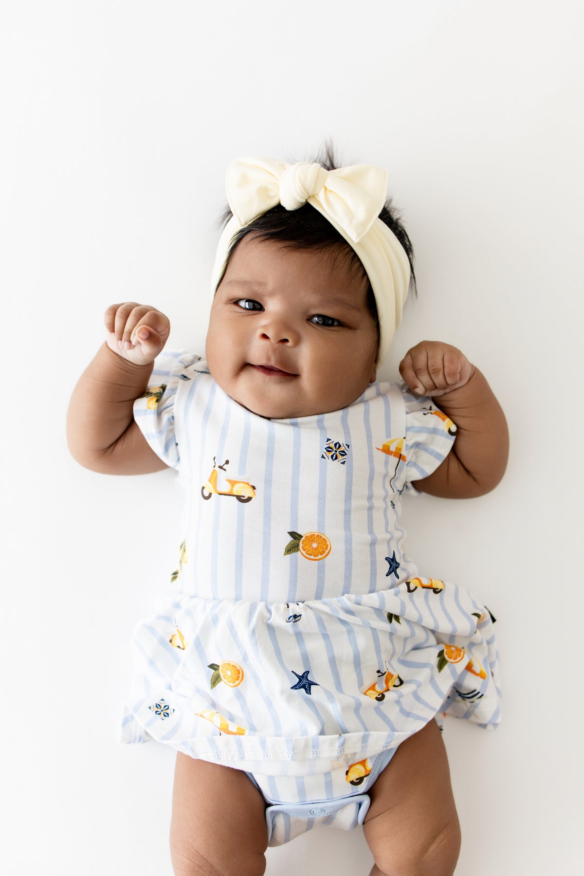 Close up of infant wearing the Twirl Bodysuit Dress in Amalfi Coast with a light yellow bow