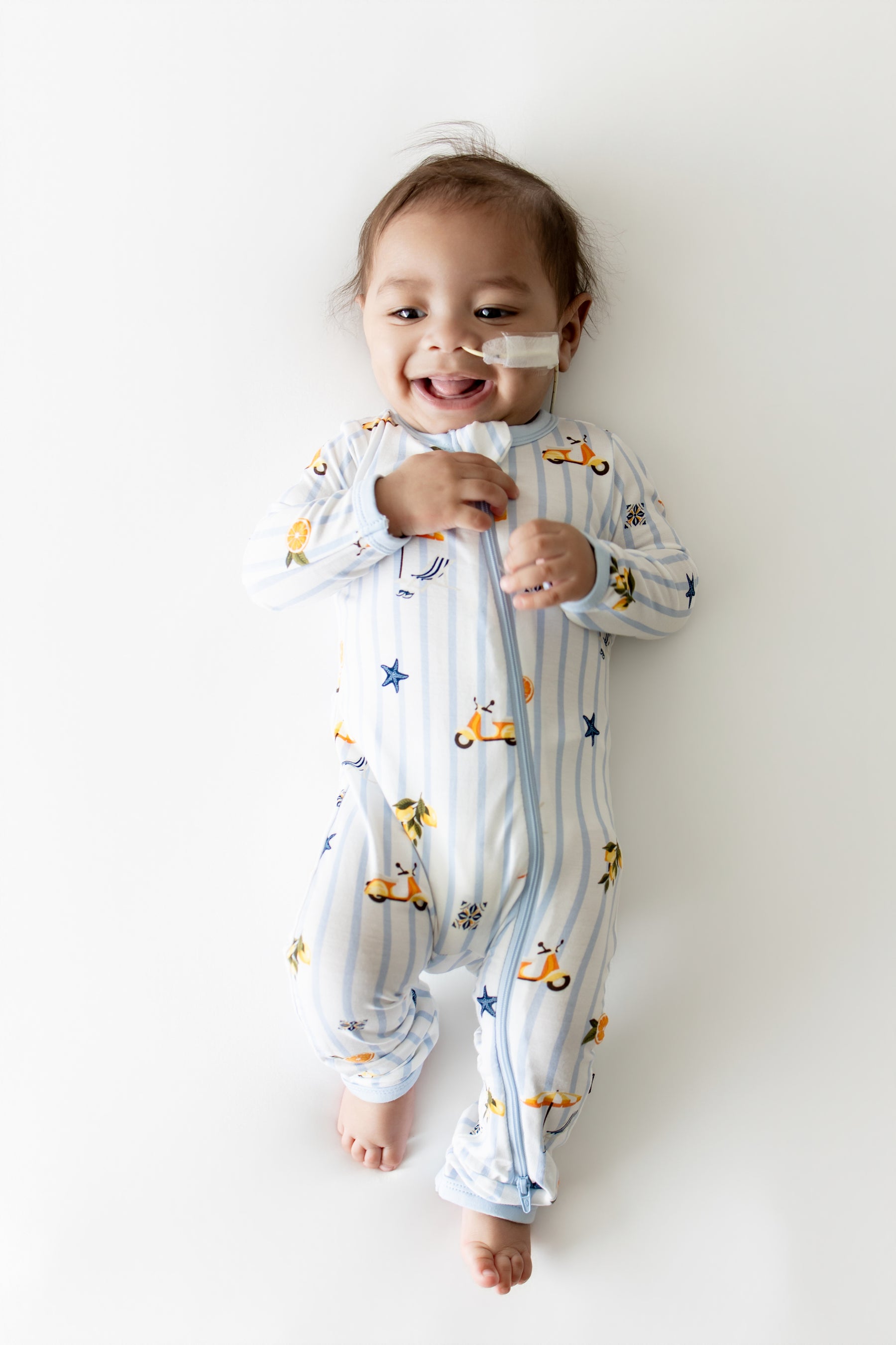 Smiling infant laying on a light surface wearing the Zippered Romper in Amalfi Coast