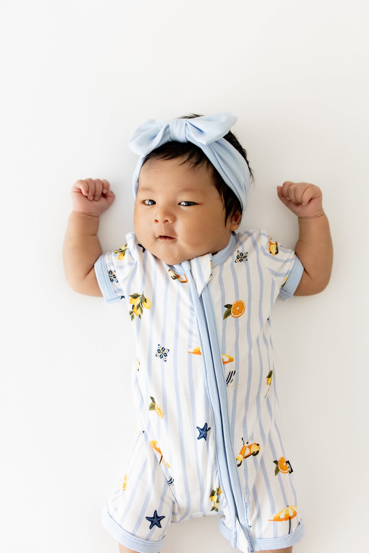 Close up of infant wearing the Zipper Shortall Romper in Amalfi Coast with a light blue bow