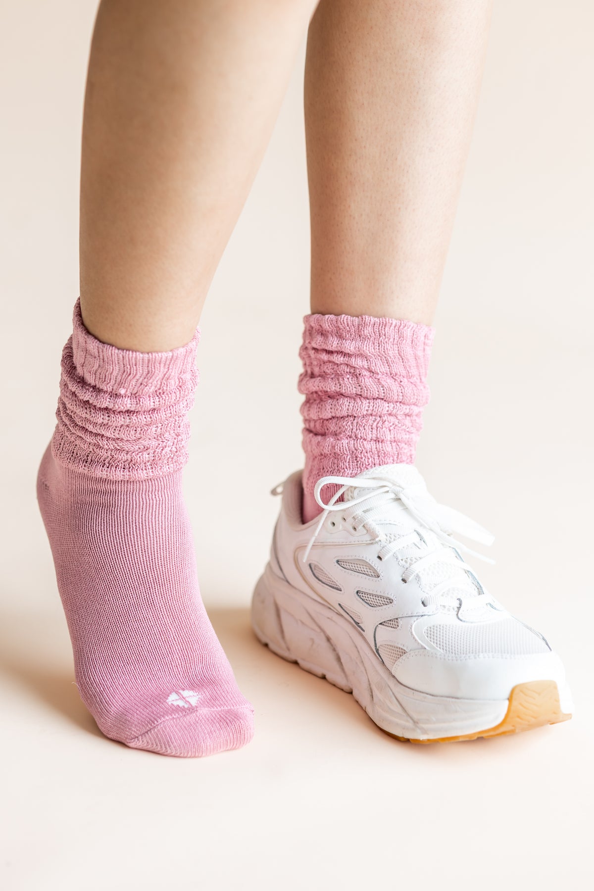 A close-up of a person's feet wearing a pair of light pink ribbed crew socks and white sneakers against a solid light beige background.