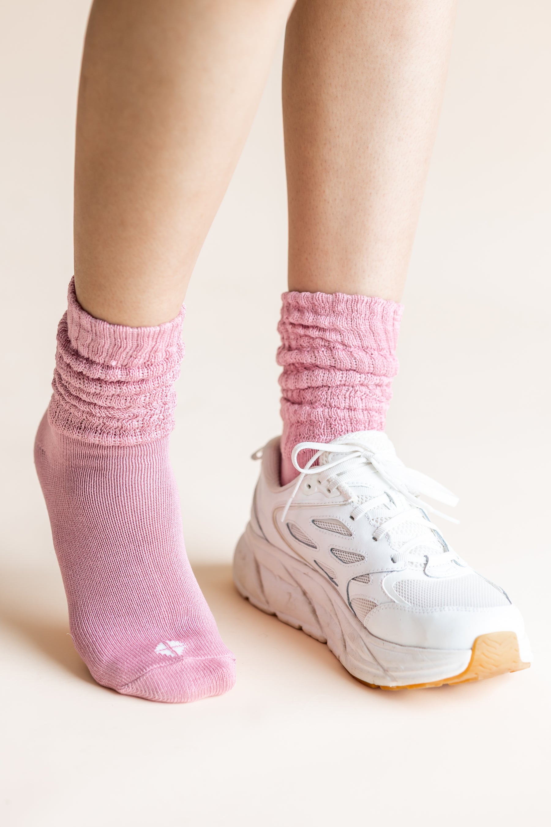 A close-up of a person's feet wearing a pair of light pink ribbed crew socks and white sneakers against a solid light beige background.