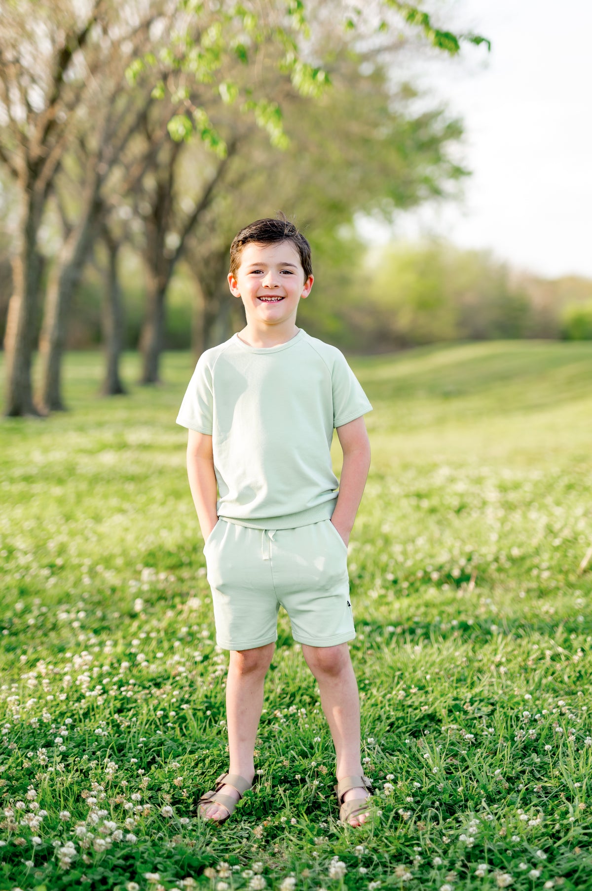 Young boy standing in a field with his hands in the shorts pocket of the Short Sleeve Jogger Set in Basil