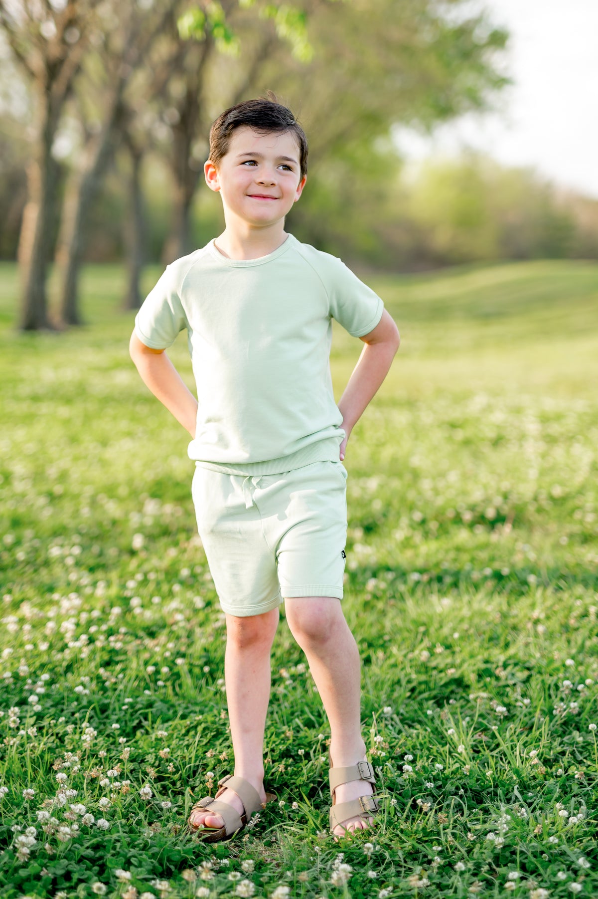 Young boy posing in a grass field wearing the Short Sleeve Jogger Set in Basil