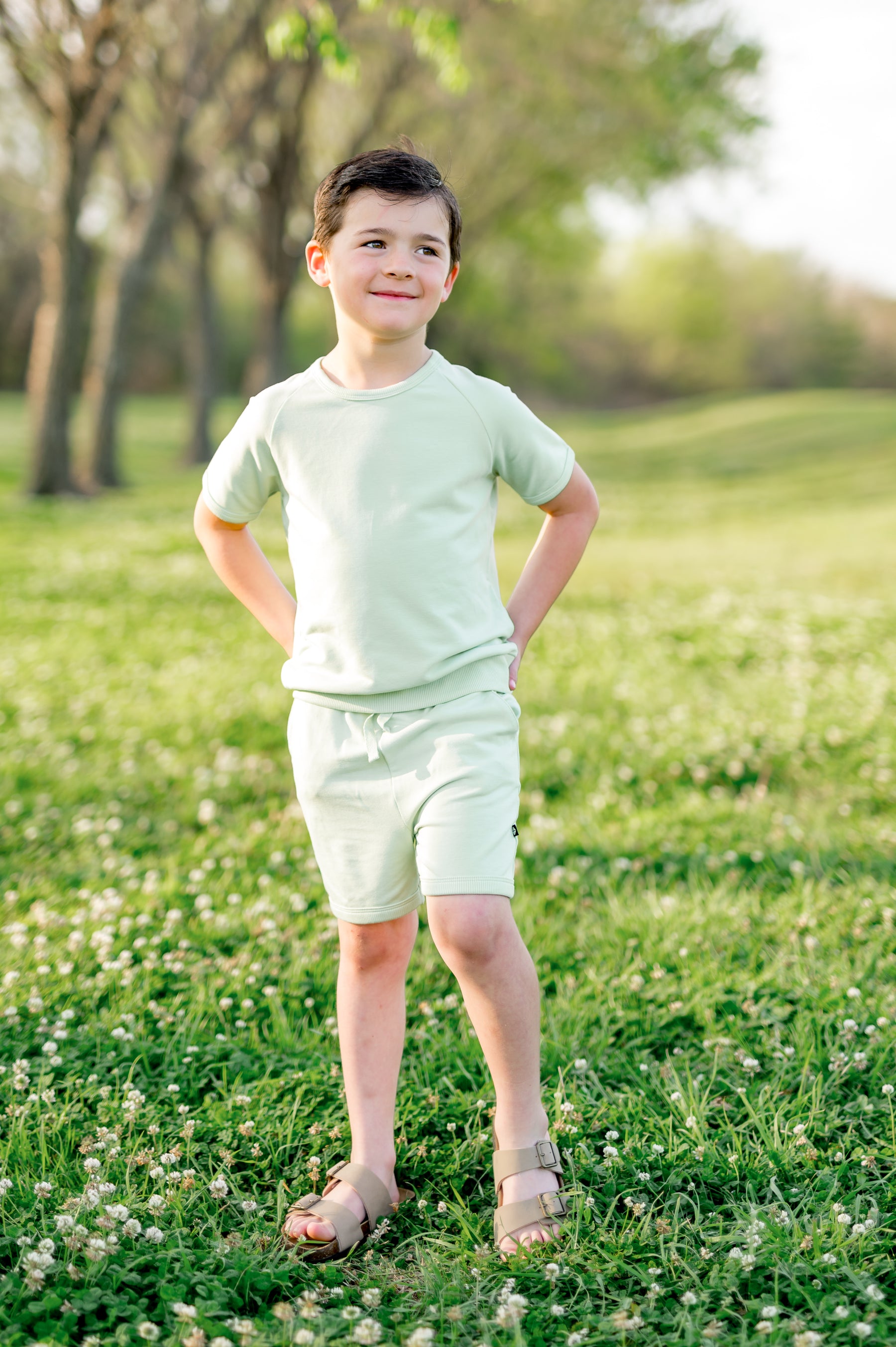 Young boy posing in a grass field wearing the Short Sleeve Jogger Set in Basil